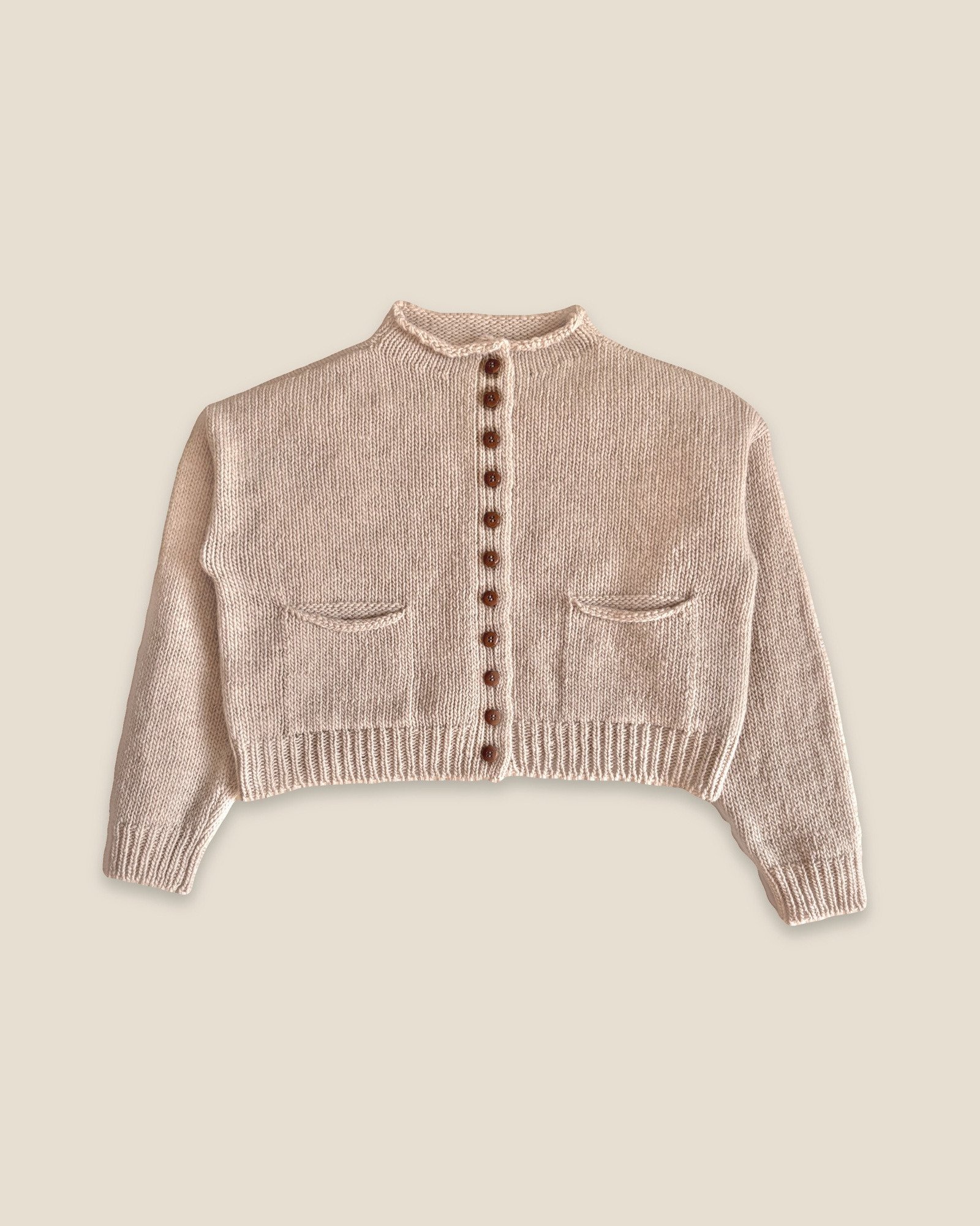 Pale Rose Pomba Cardigan by Floca, handcrafted in Galicia from Spanish wool, laid flat with a button front, two patch pockets and ribbed cuffs and hem.