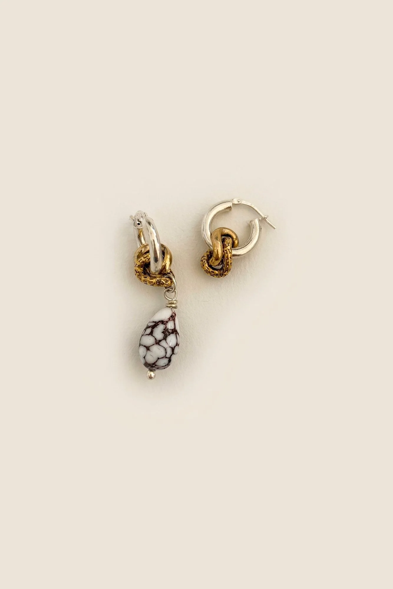Asymmetric pair of silver hoop earrings with linked gold-plated rings, one hoop with a white and brown crackle-glazed ceramic drop