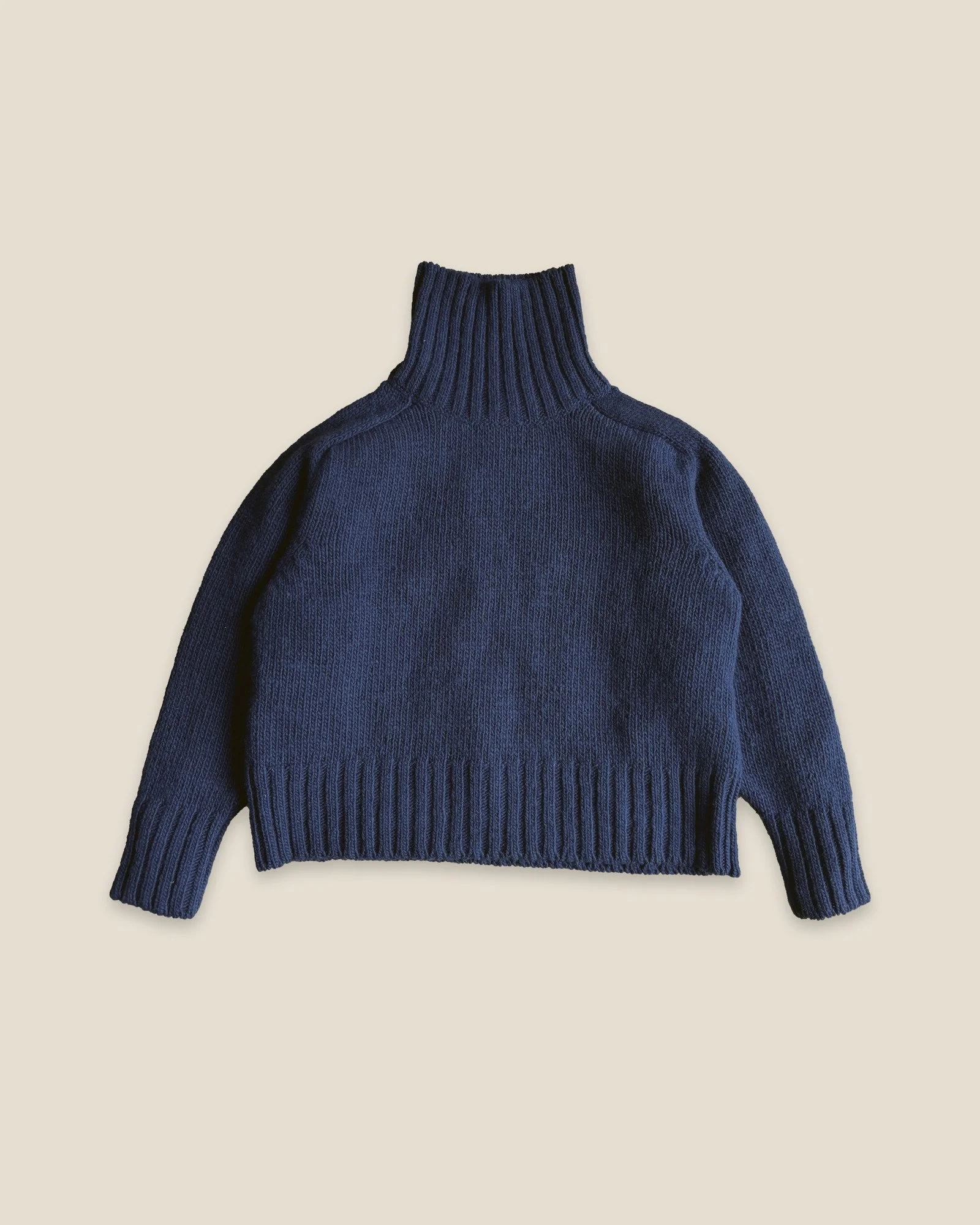 Floca Ringo Sweater in ink blue, laid flat, with the turtleneck standing up and ribbed cuffs and hem