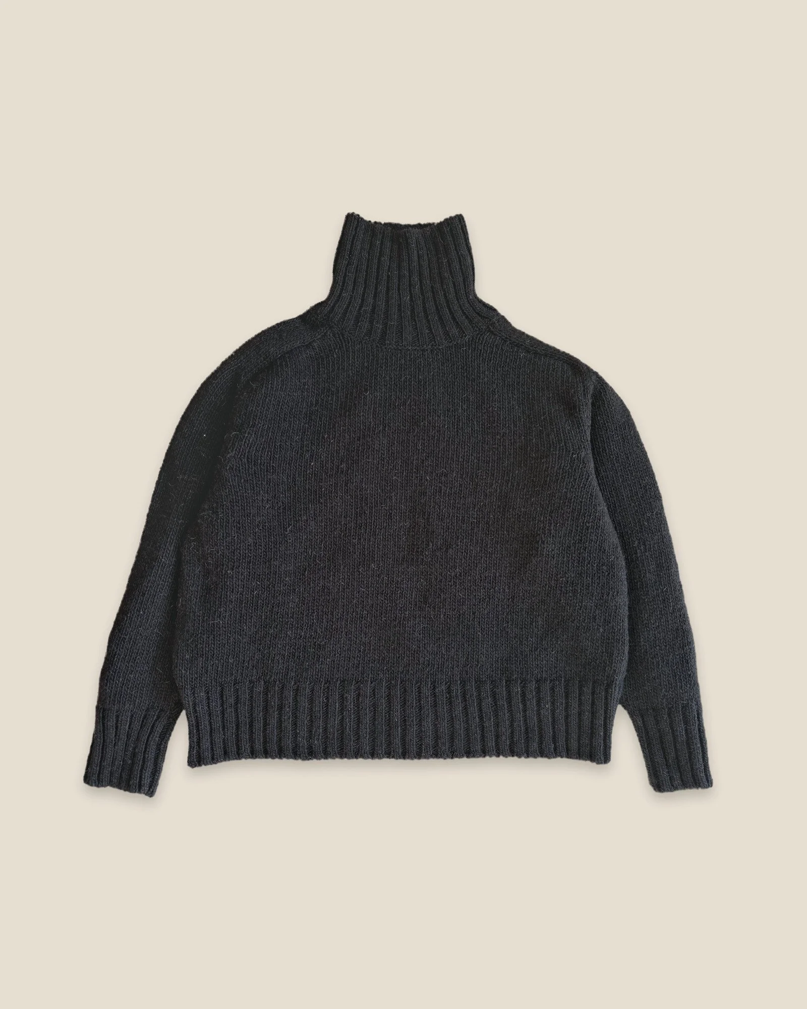 Black Ringo Oversize Sweater by Floca, handcrafted in Galicia from Spanish wool, laid flat with the tall turtleneck up and ribbed cuffs and hem.
