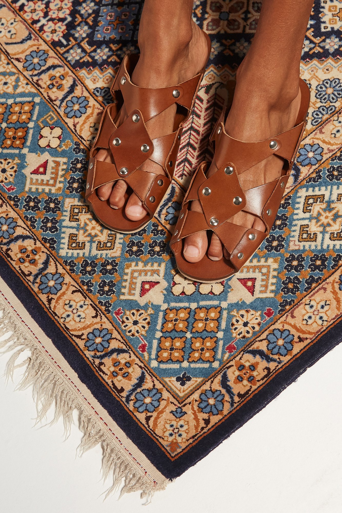 Cordoa Muscari sandal in brown, close-up of the studded leather crossover straps worn on a patterned rug