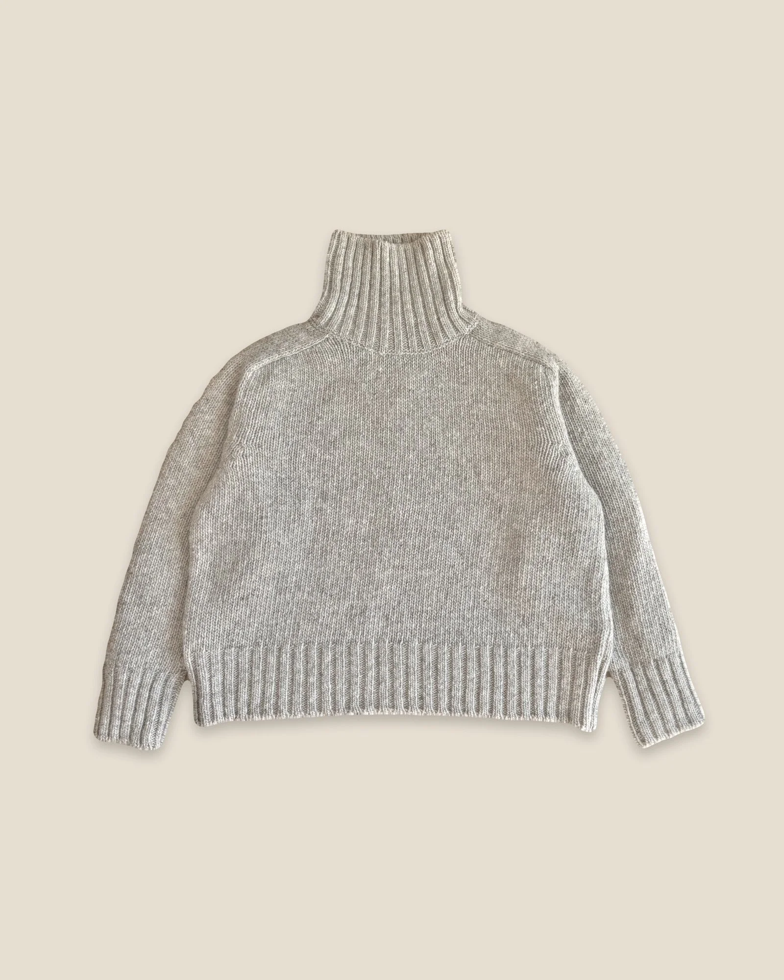 Fog Grey Ringo Oversize Sweater by Floca, handcrafted in Galicia from Spanish wool, laid flat with the tall turtleneck up and ribbed cuffs and hem.