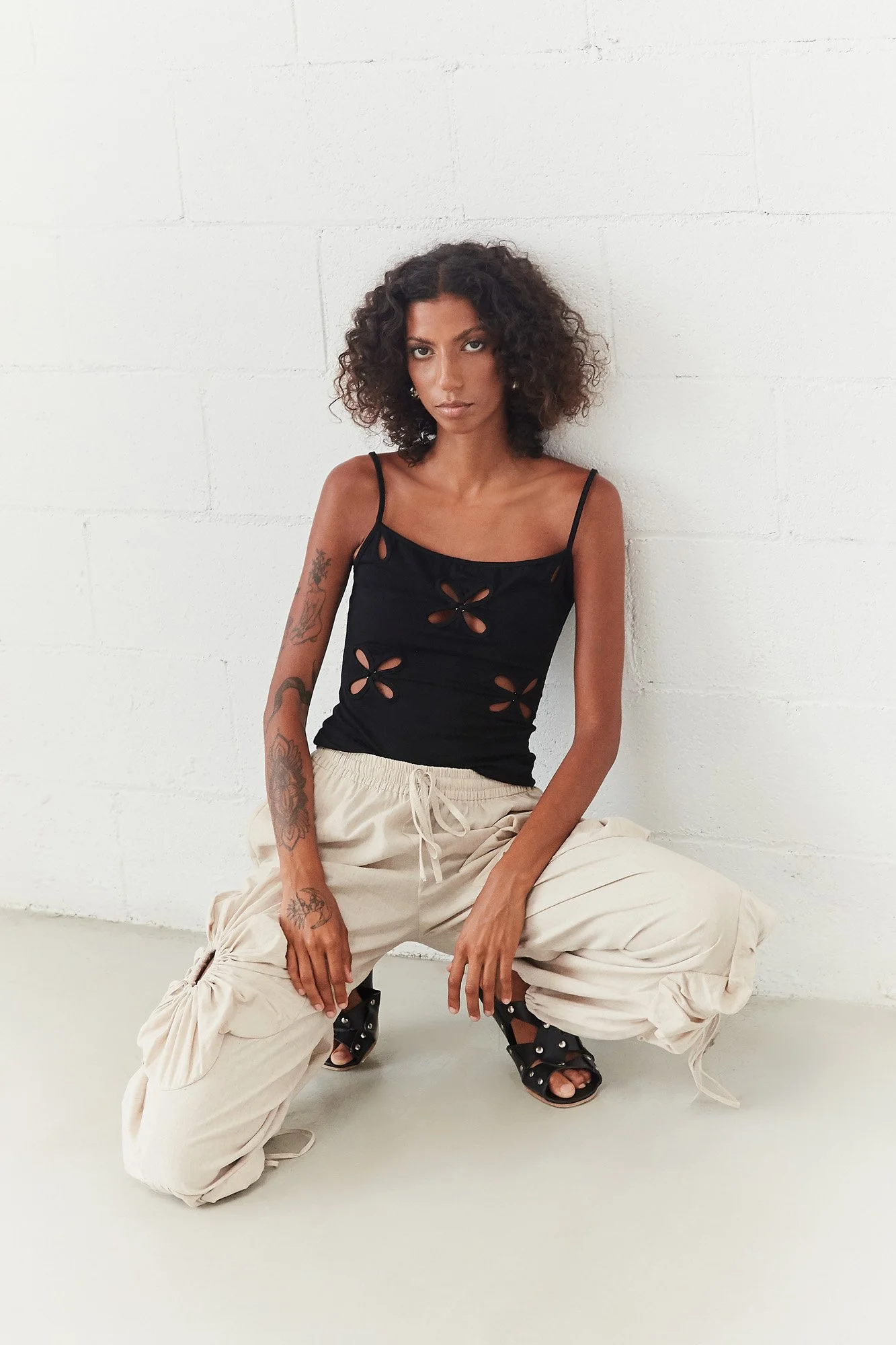 Model wearing the J.Kim Chilla black camisole with linen cream trousers, seated full-length view