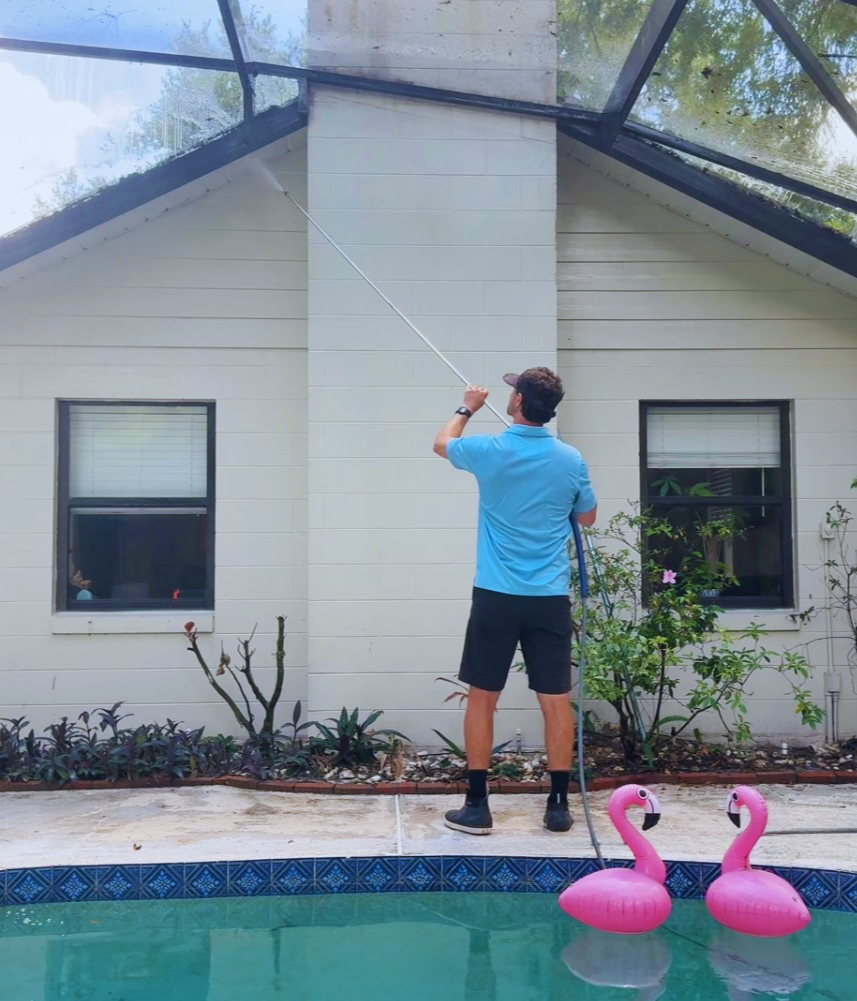 Technician from Honey Do Exterior Cleaning soft washing screened pool enclosure and patio area in Central Florida using extension pole for safe, effective residential exterior cleaning