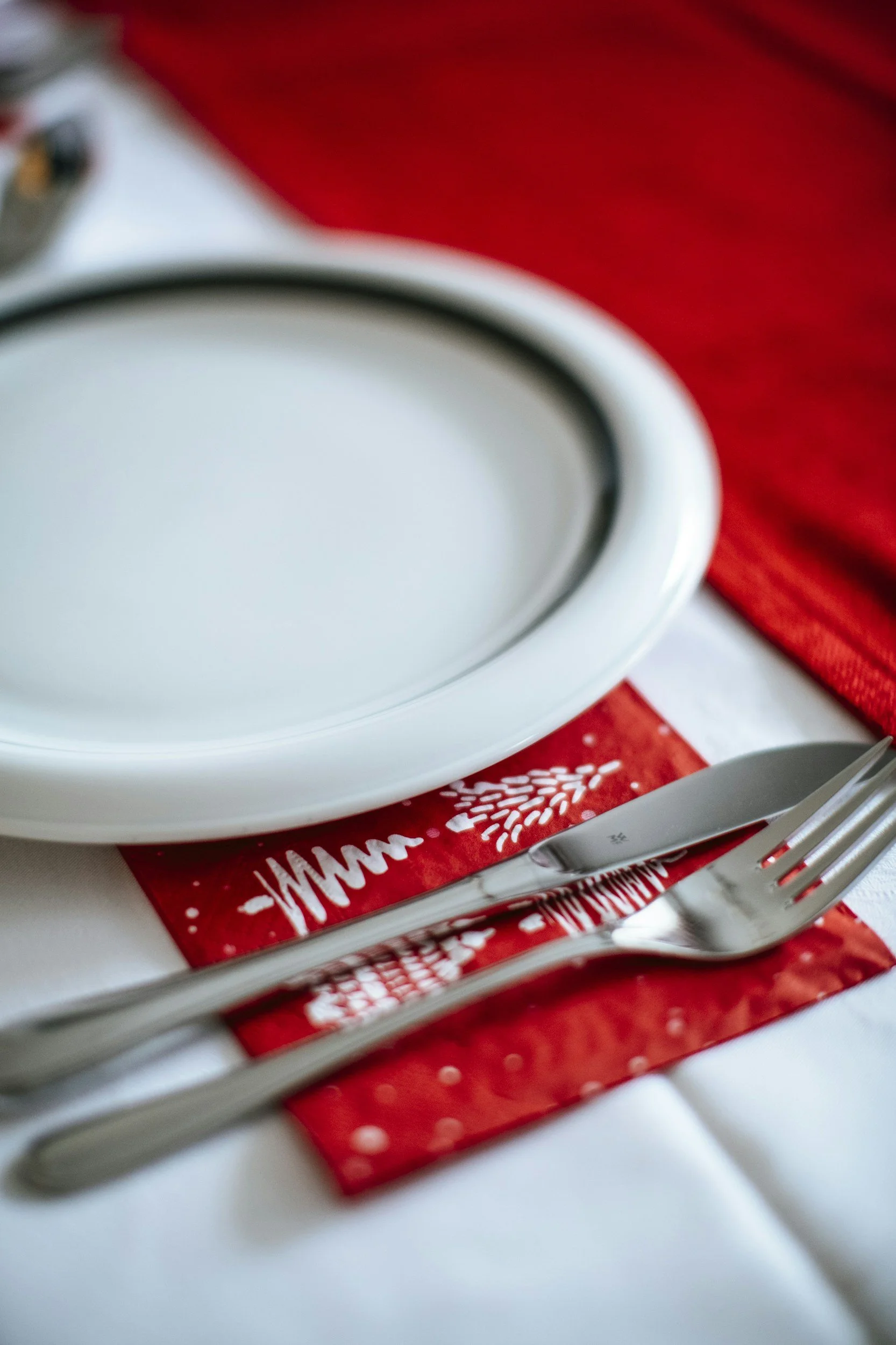 Ein weißer Teller, Besteck und eine rote Weihnachtsserviette mit weißen Schneeflocken auf einem Tisch.