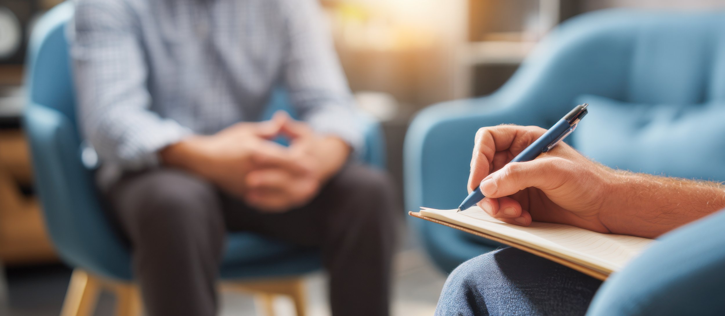 A counselor or therapist taking notes while talking to a patient in a therapy session in a modern office.