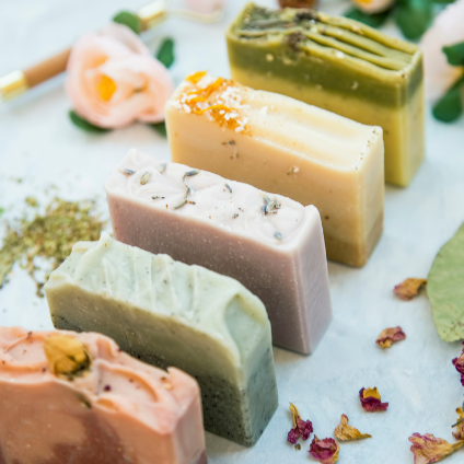 Four pieces of handmade soap with various colors and textures, decorated with flower petals and leaves, on a white surface.