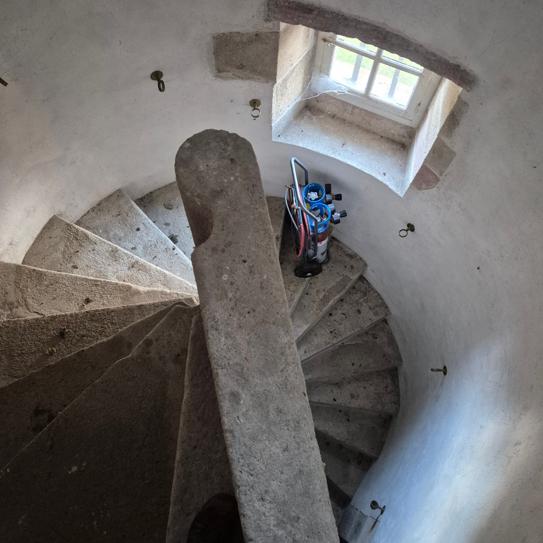 Escalier en pierre dans une tour avec une fenêtre laissant entrer de la lumière, une bouteille de gaz avec des outils dessus.