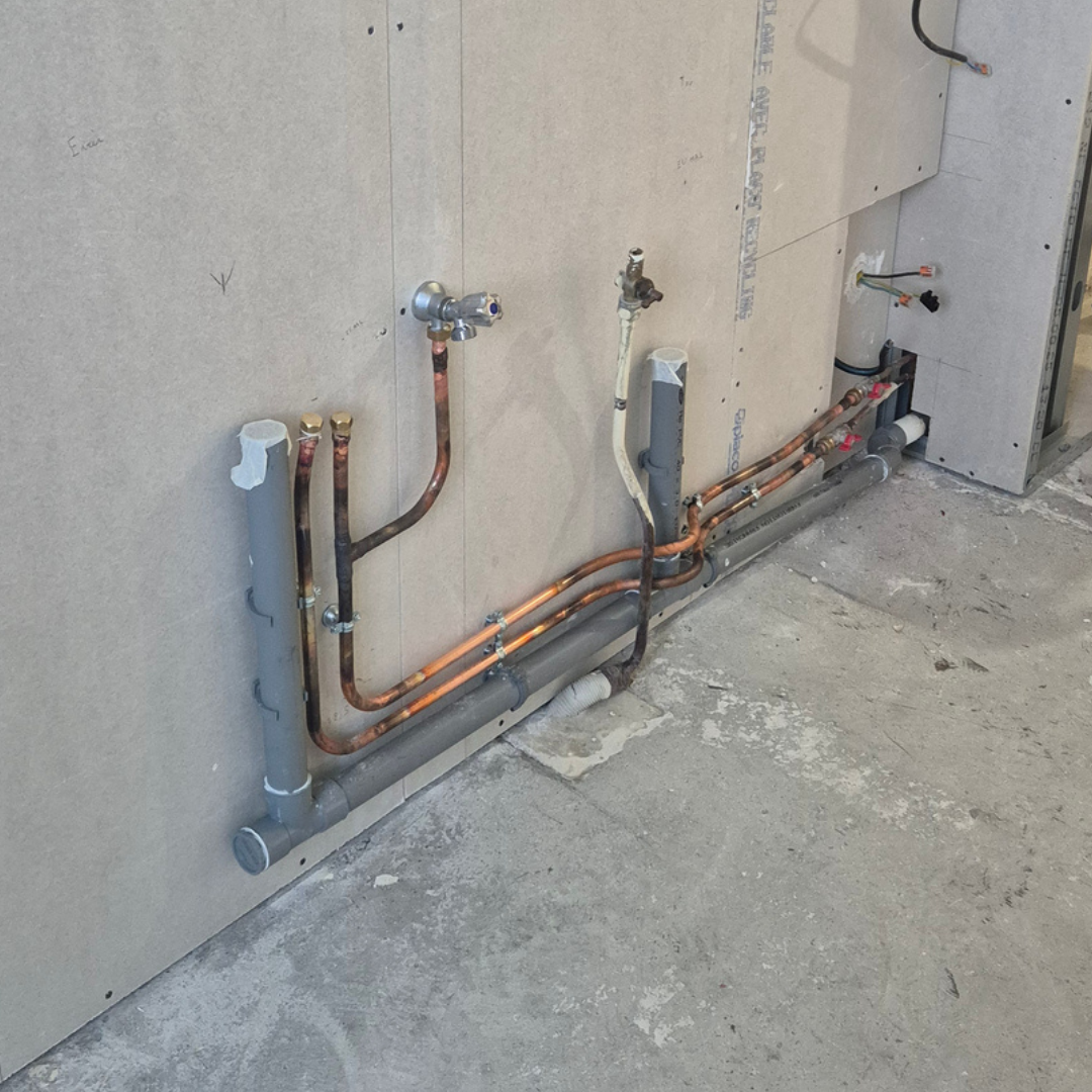 Installation de plomberie avec tuyaux en cuivre et en PVC fixés à un mur en construction.