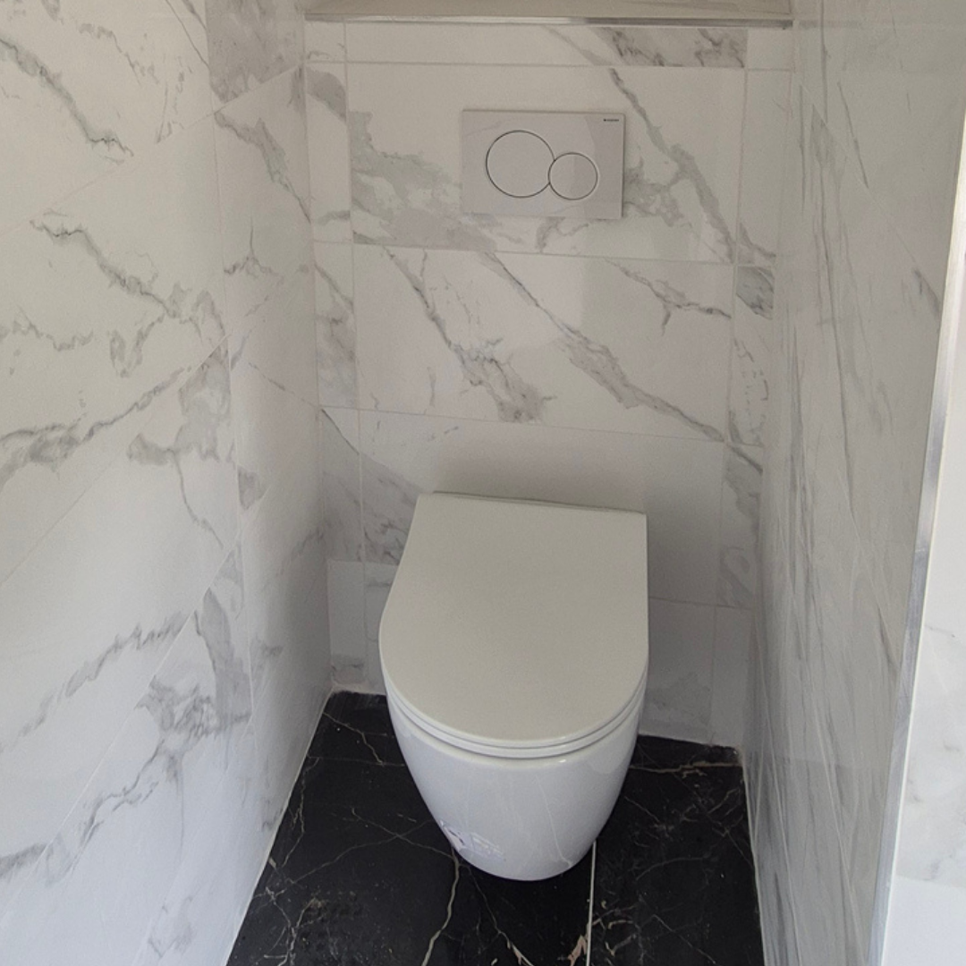 Toilettes modernes avec un système de chasse intégré dans un mur en marbre blanc avec veines grises, sur un sol en marbre noir.