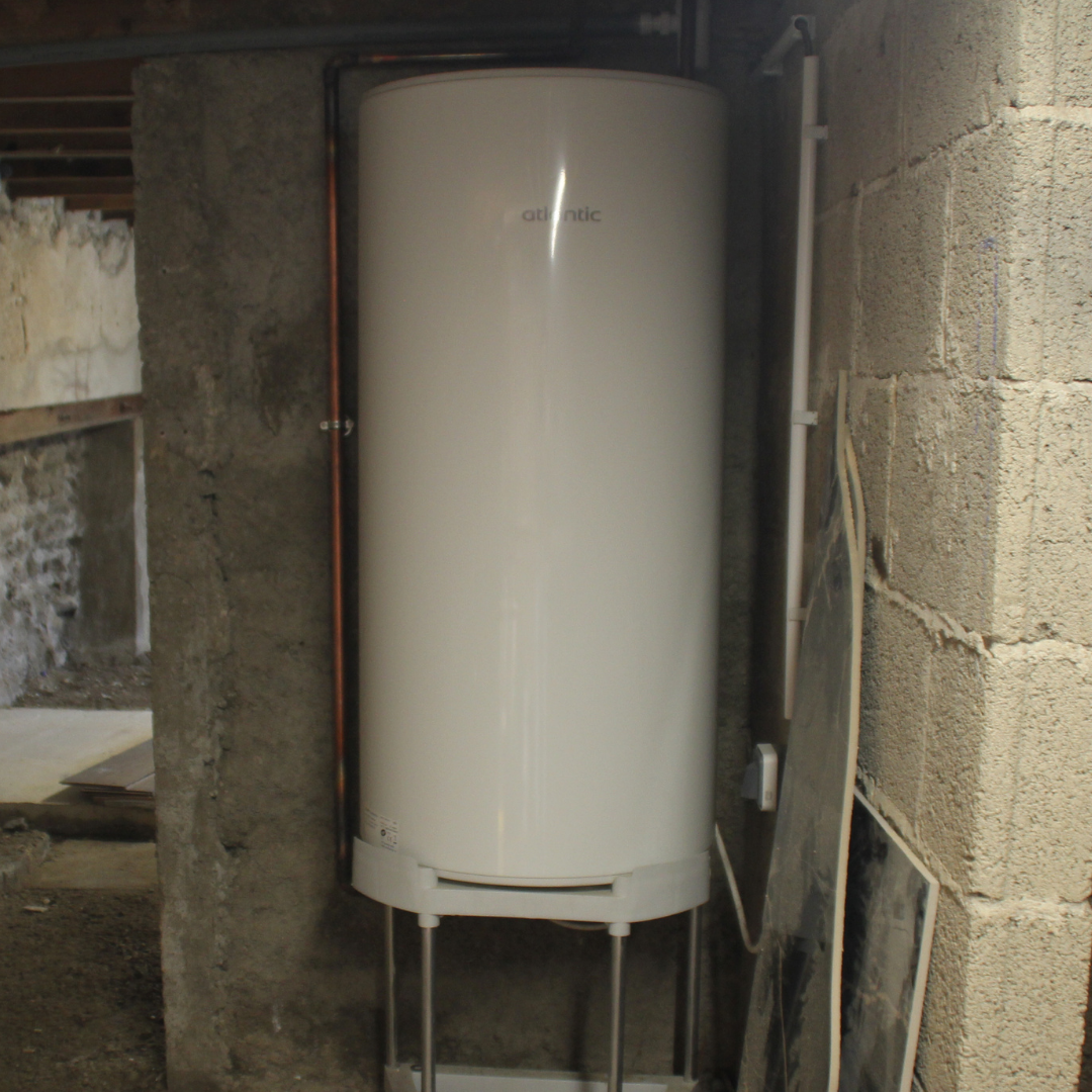 Chauffe-eau blanc installé dans un mur en construction avec des murs en béton et quelques panneaux à côté.