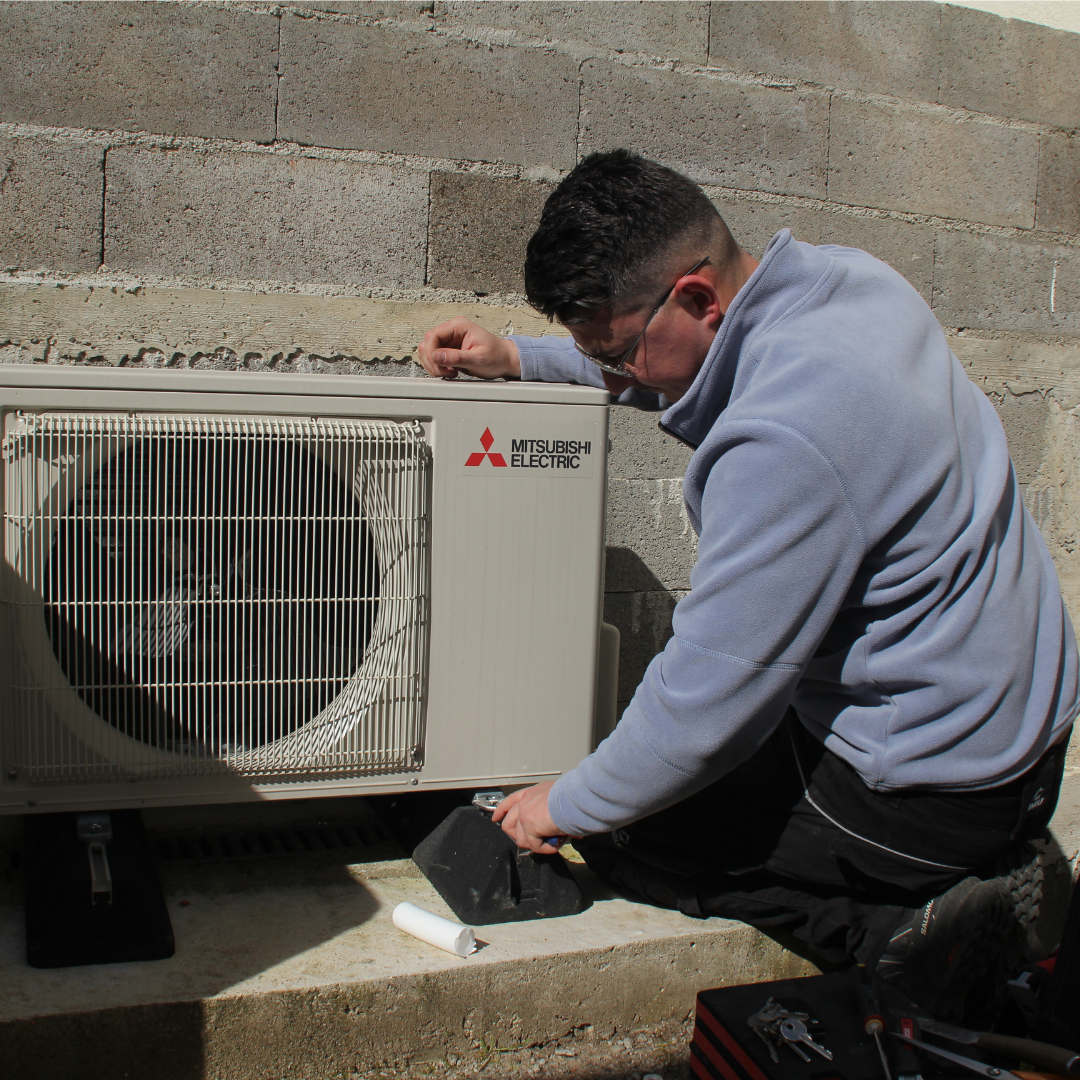 Un technicien répare une unité de climatisation Mitsubishi Electric à l'extérieur.