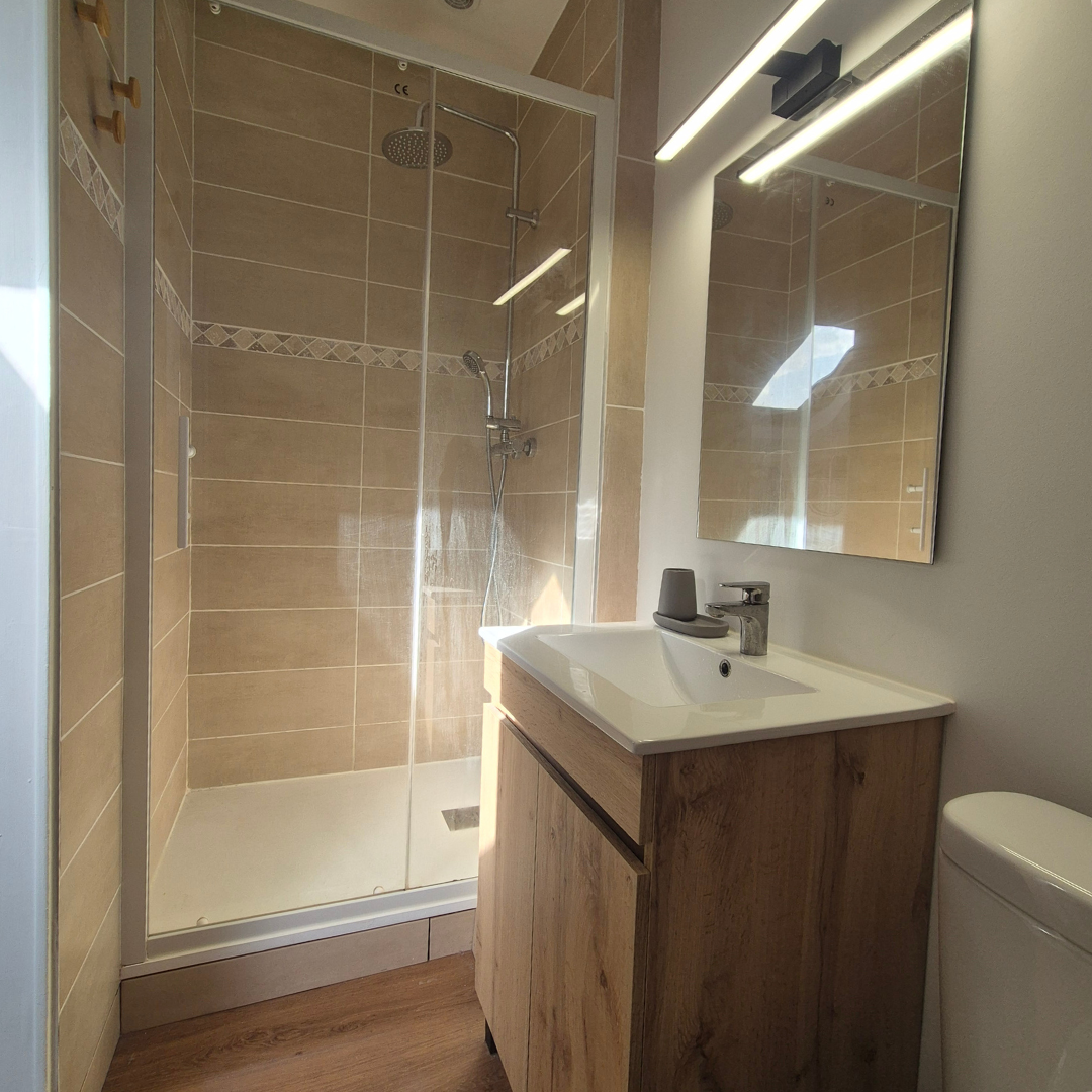 Petite salle de bain avec douche en verre, lavabo avec meuble en bois, miroir et toilette