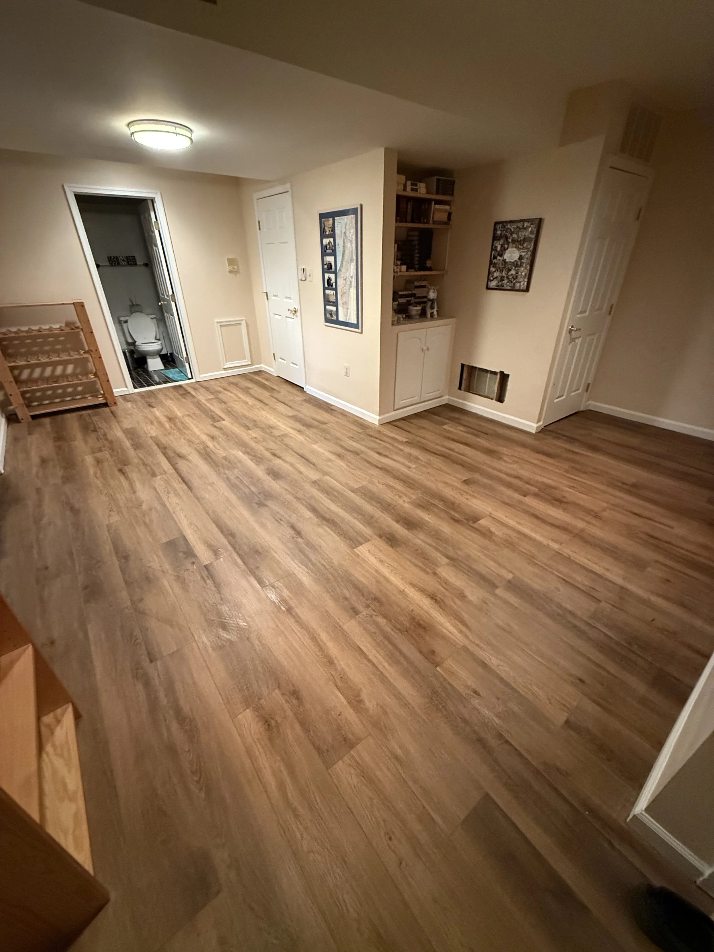 Finished open living area with warm brown wood-look plank flooring and matching stair treads.