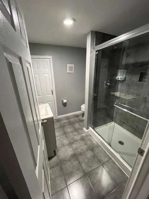 Modern bathroom remodel with glass shower enclosure, gray tile flooring, and updated fixtures in Northeast Philadelphia PA