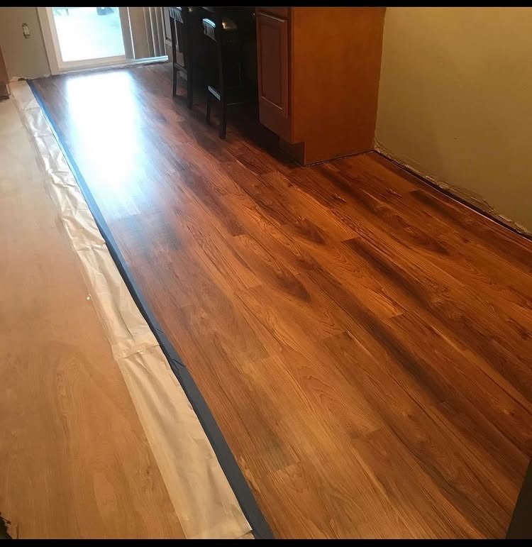 Wood-look plank flooring being installed beside a protected work area near the kitchen.