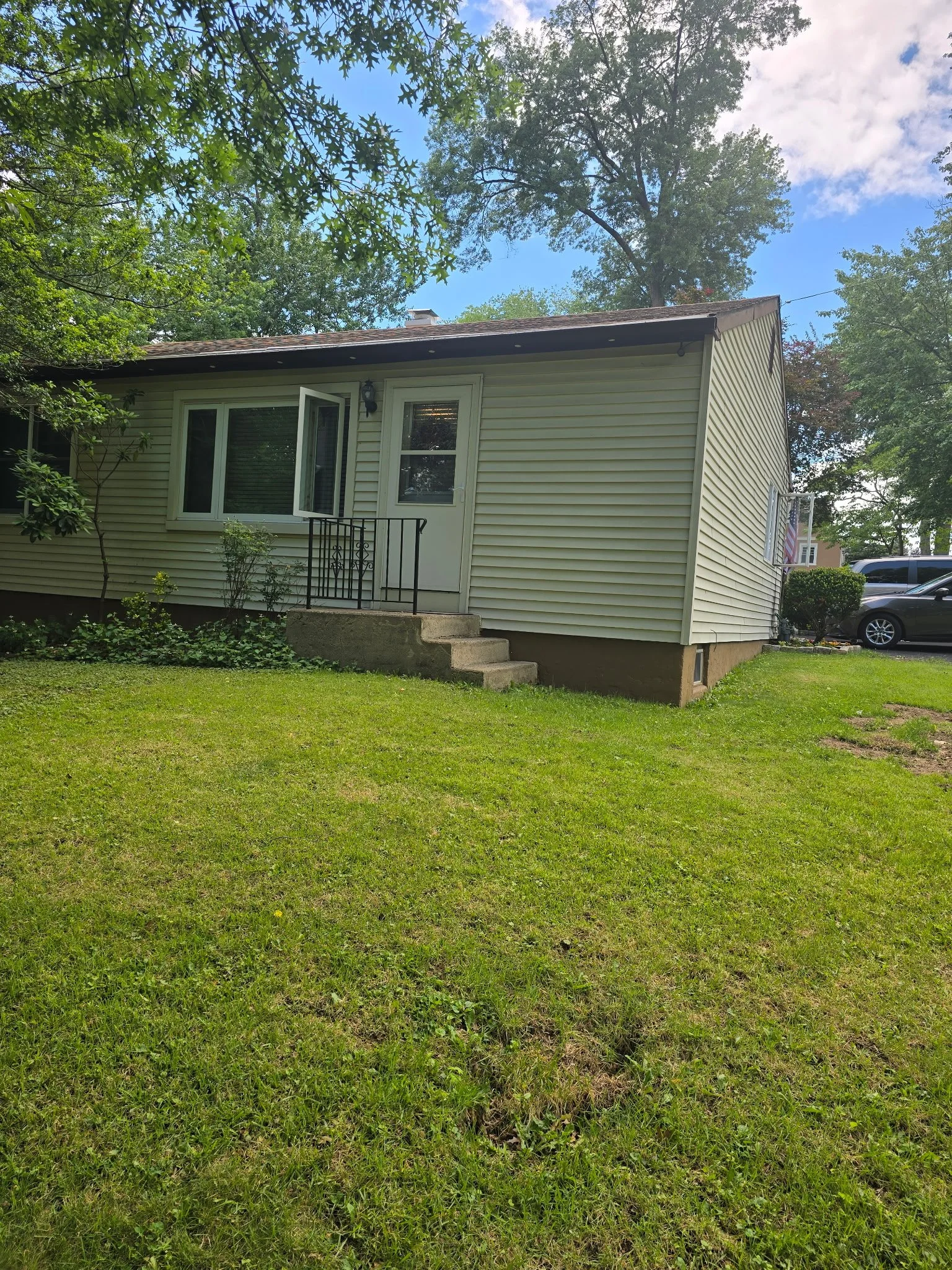 Single-story home exterior with light siding, front steps, and black metal railing.