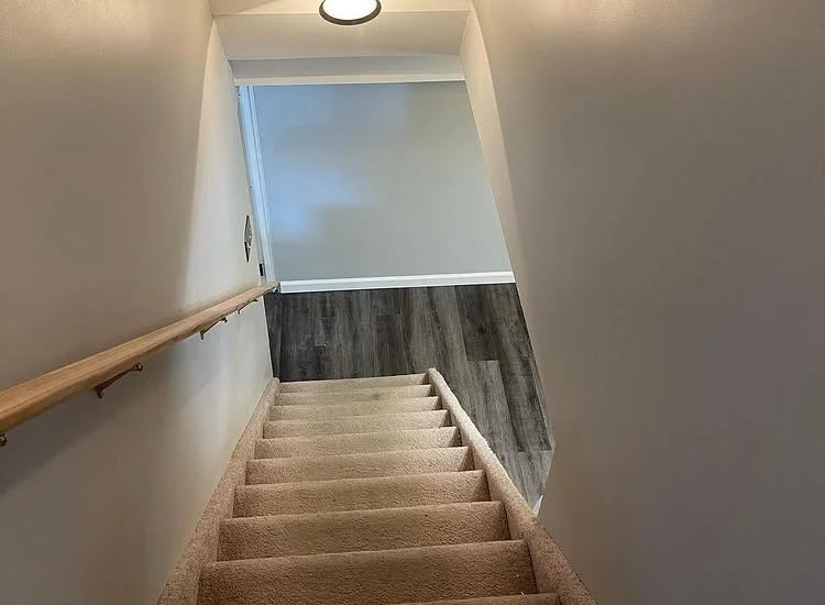 Stair landing finished with gray wood-look plank flooring beside carpeted stairs.