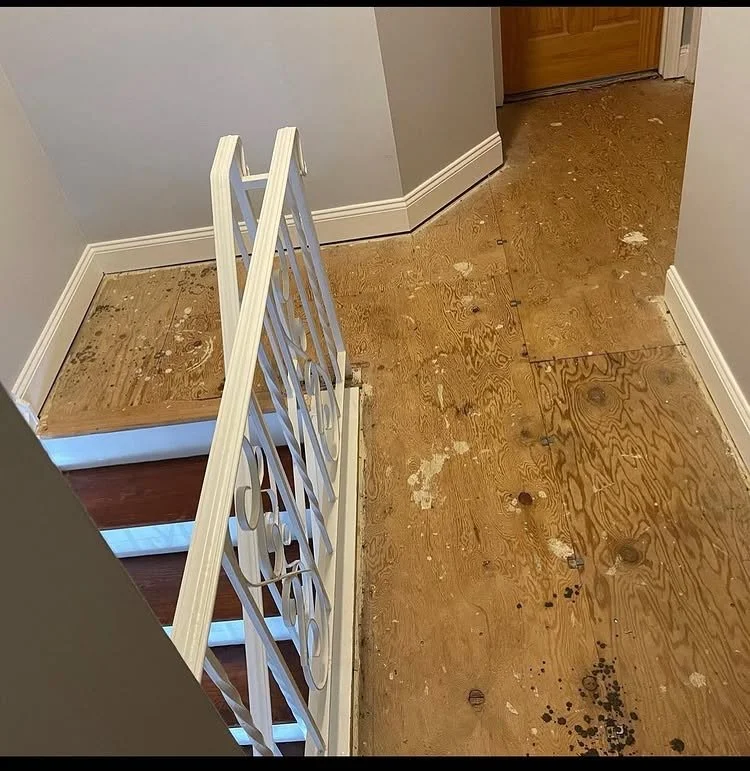 Hallway and stair landing with old flooring removed to expose the plywood subfloor.