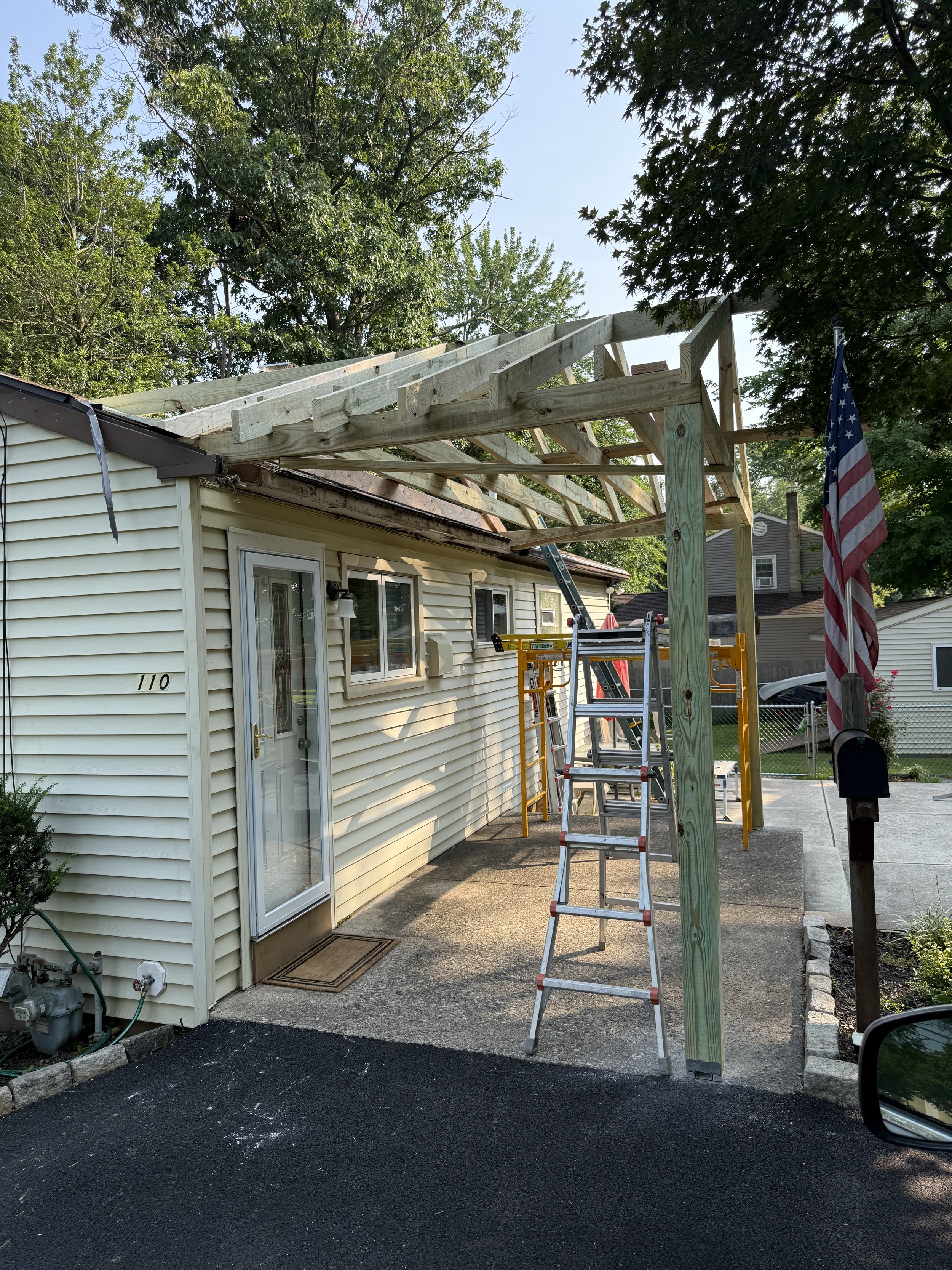 Wood porch-roof framing attached to the rear of a light-sided home during construction.