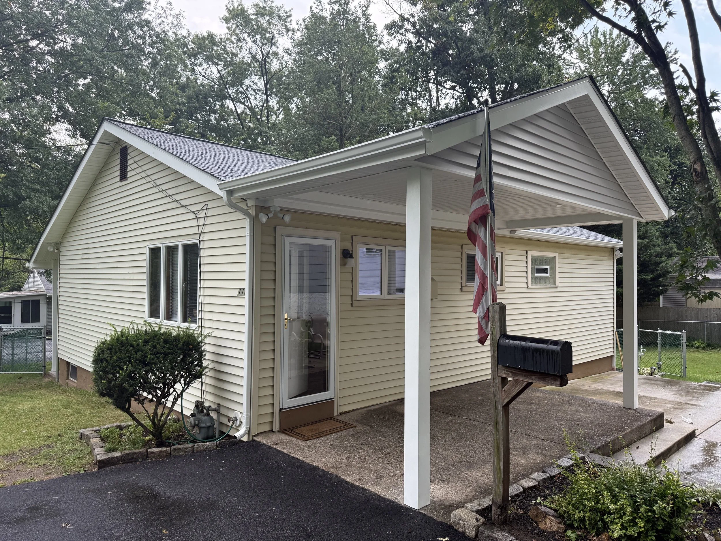 Completed gabled porch roof with white posts over a rear entry and concrete patio.