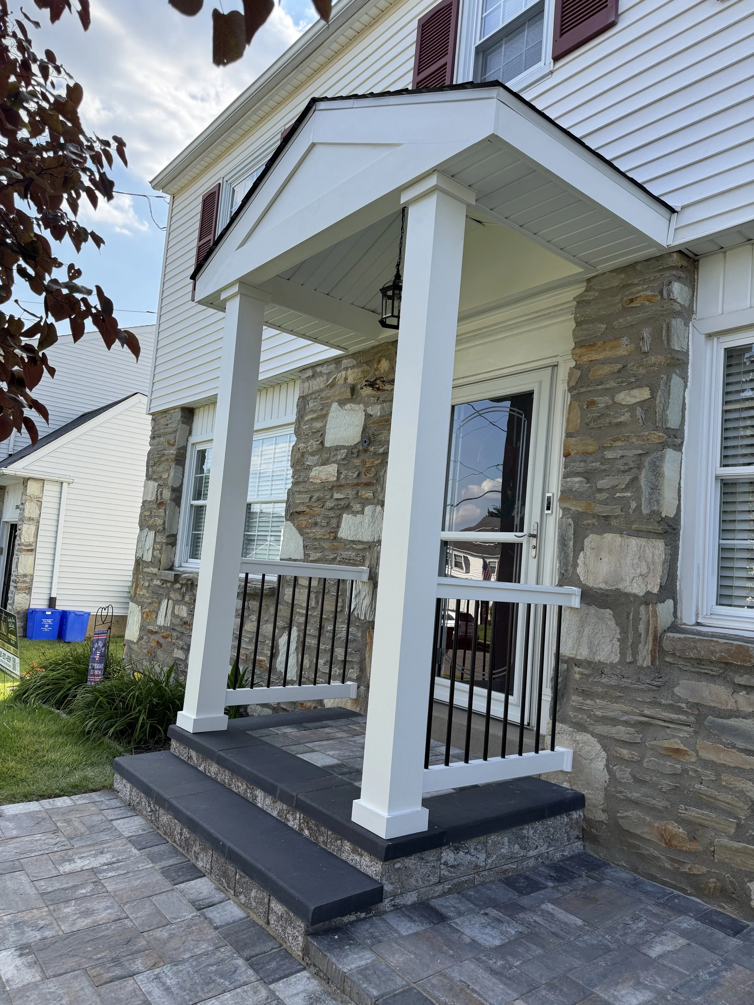Completed front entry portico with white columns, black railings, and gray steps on a stone-front home.