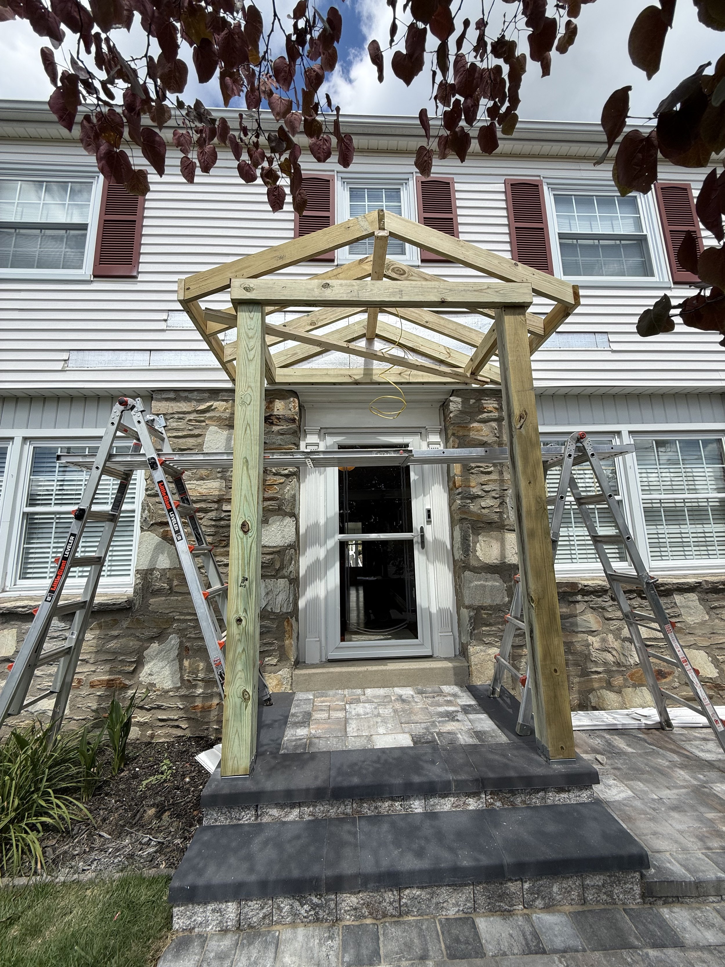 Wood framing for a new front entry portico attached to a stone-front home.