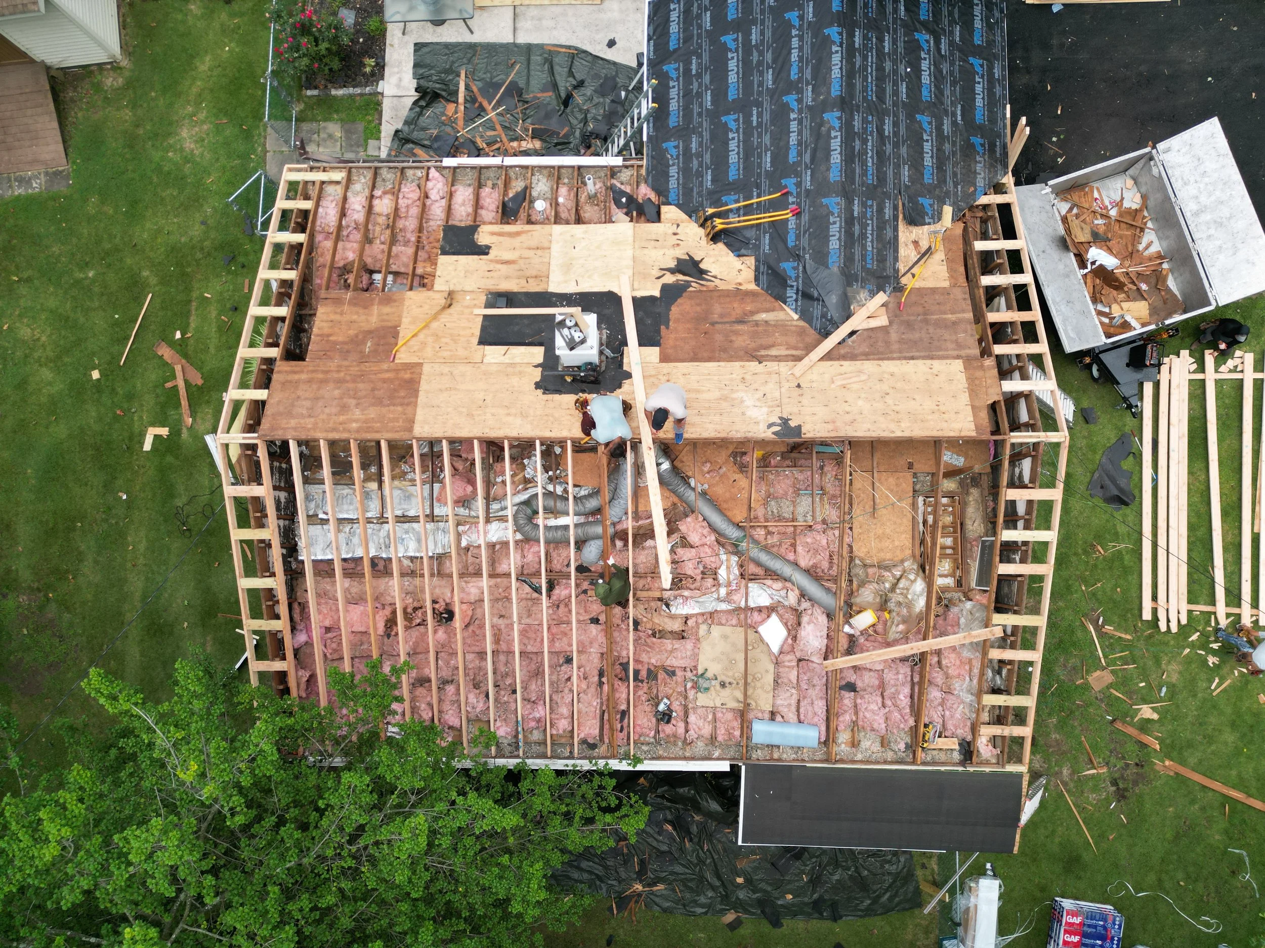 Aerial view of open wood framing and plywood roof sheathing during exterior construction.