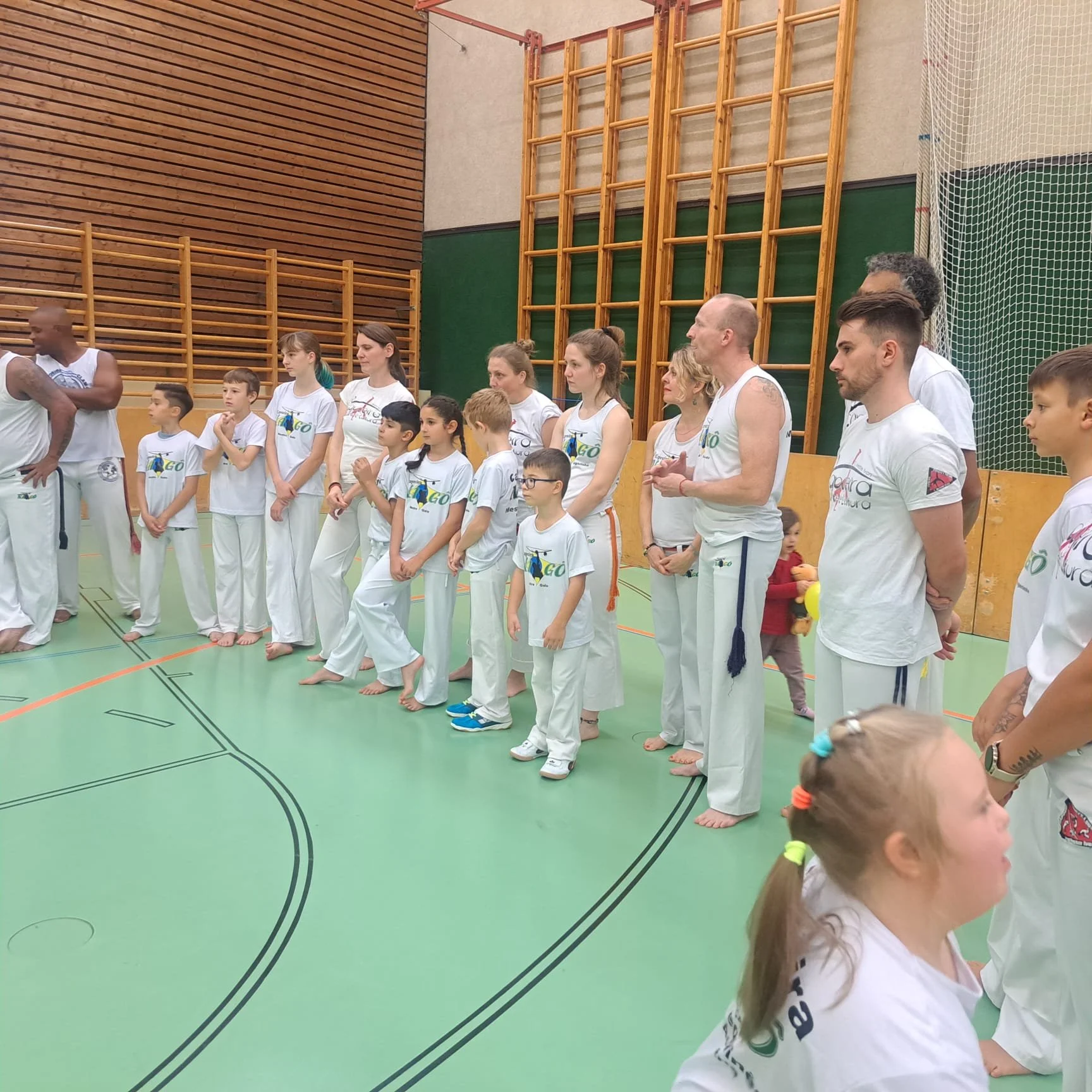 Eine Gruppe von Menschen in weißen Sportanzügen, die in einer Turnhalle stehen, sich auf eine Veranstaltung oder ein Training vorbereiten und sich anschauen.