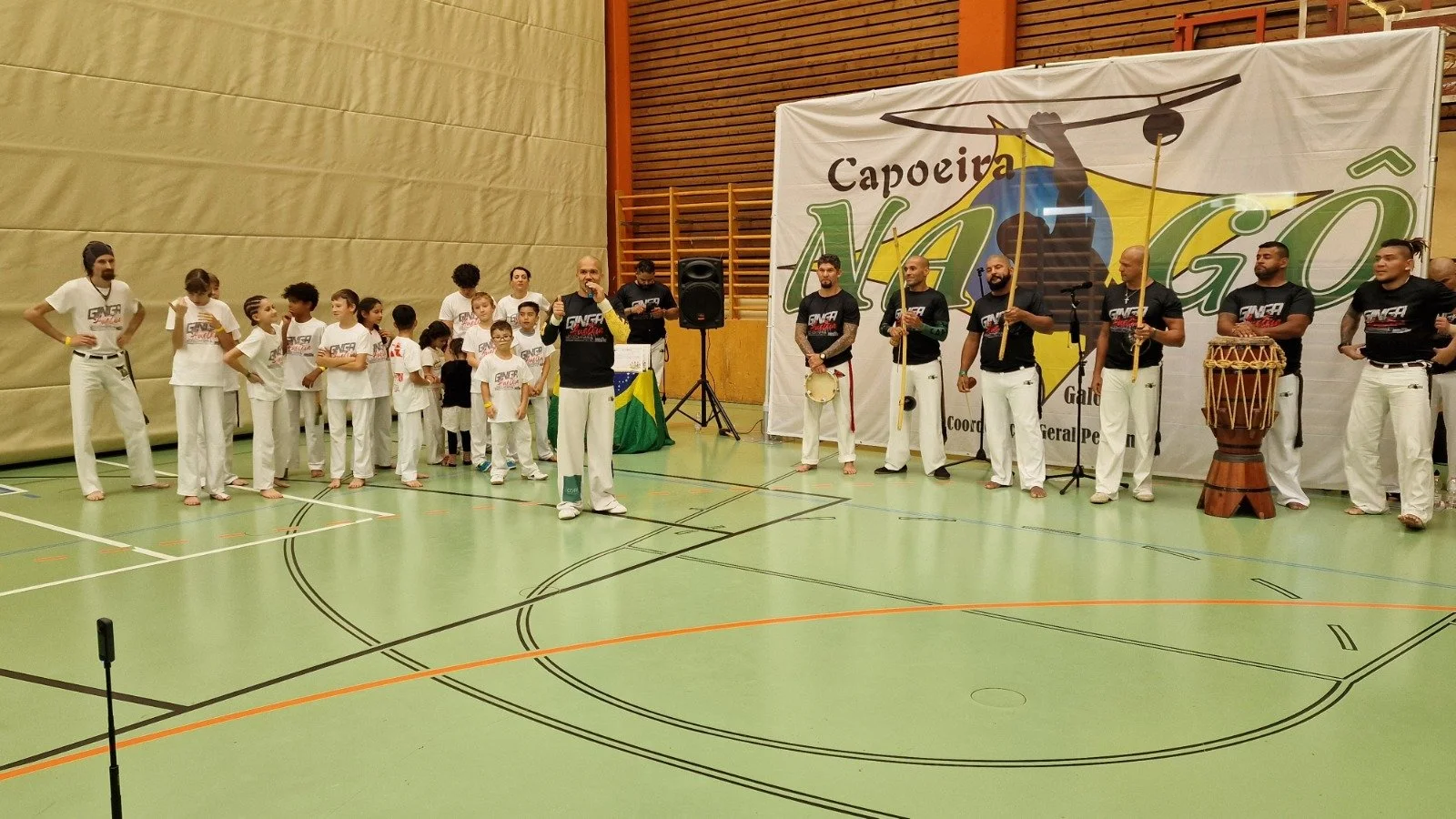 Gruppe von Capoeira-Künstlern und Kindern, die in einer Sporthalle an einem Capoeira-Event teilnehmen.