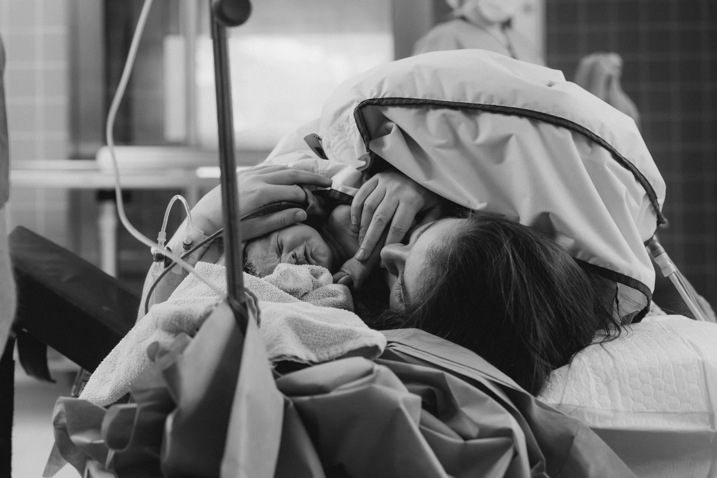 Schwangere Frau im Kreißsaal liegt im Krankenbett, umgeben von medizinischem Personal, während die Wehen einsetzen.