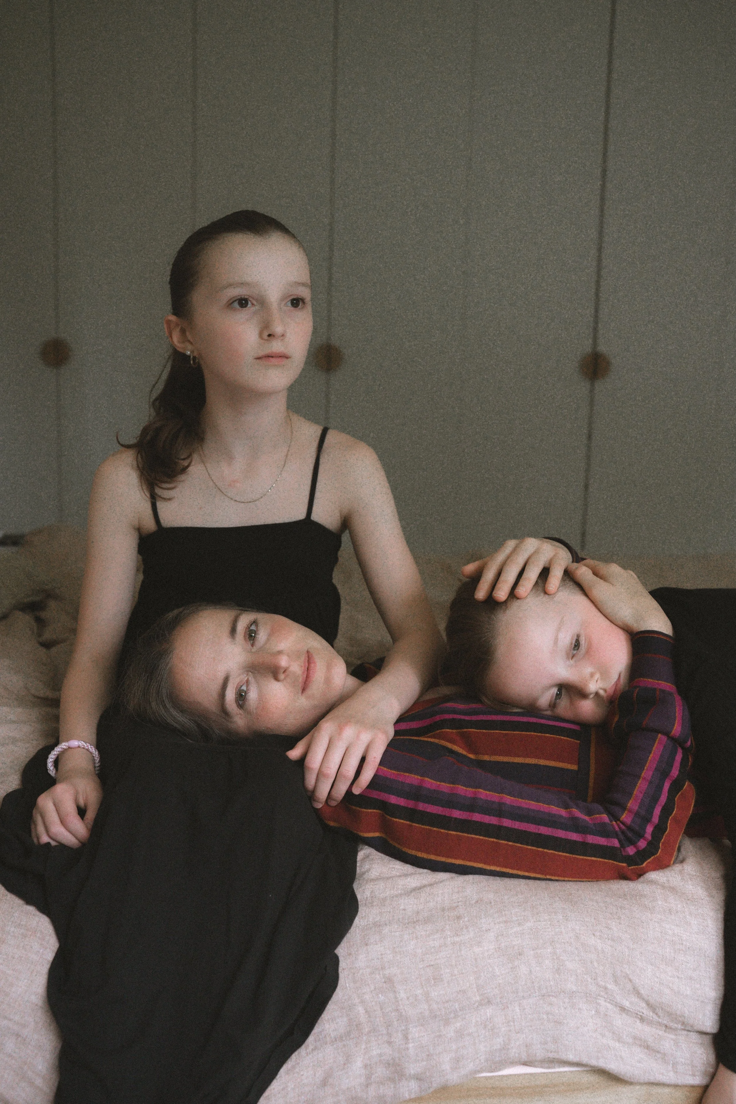 Drei junge Menschen kuscheln zusammen auf einem Bett, eine Person sitzt und hält die anderen beiden, die liegen, in einem gemütlichen Raum.