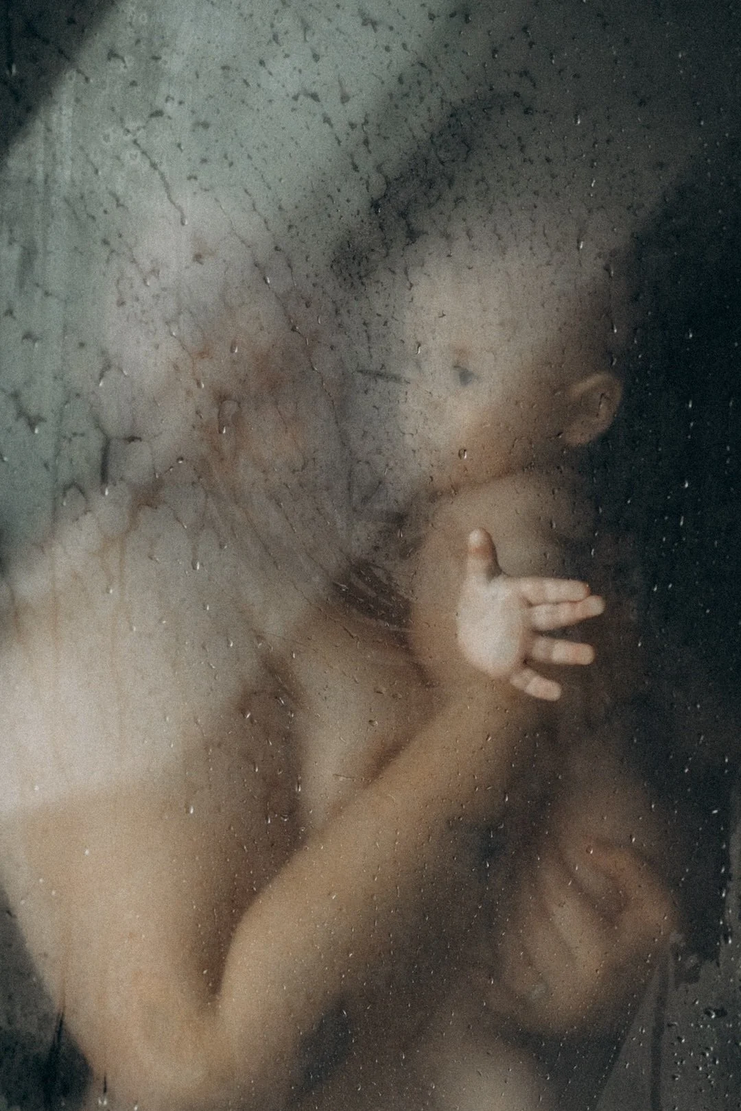 Kleines Kind hinter einer glasigen, nassen Glasscheibe, die Wassertröpfchen hat, und streckt eine Hand gegen das Glas