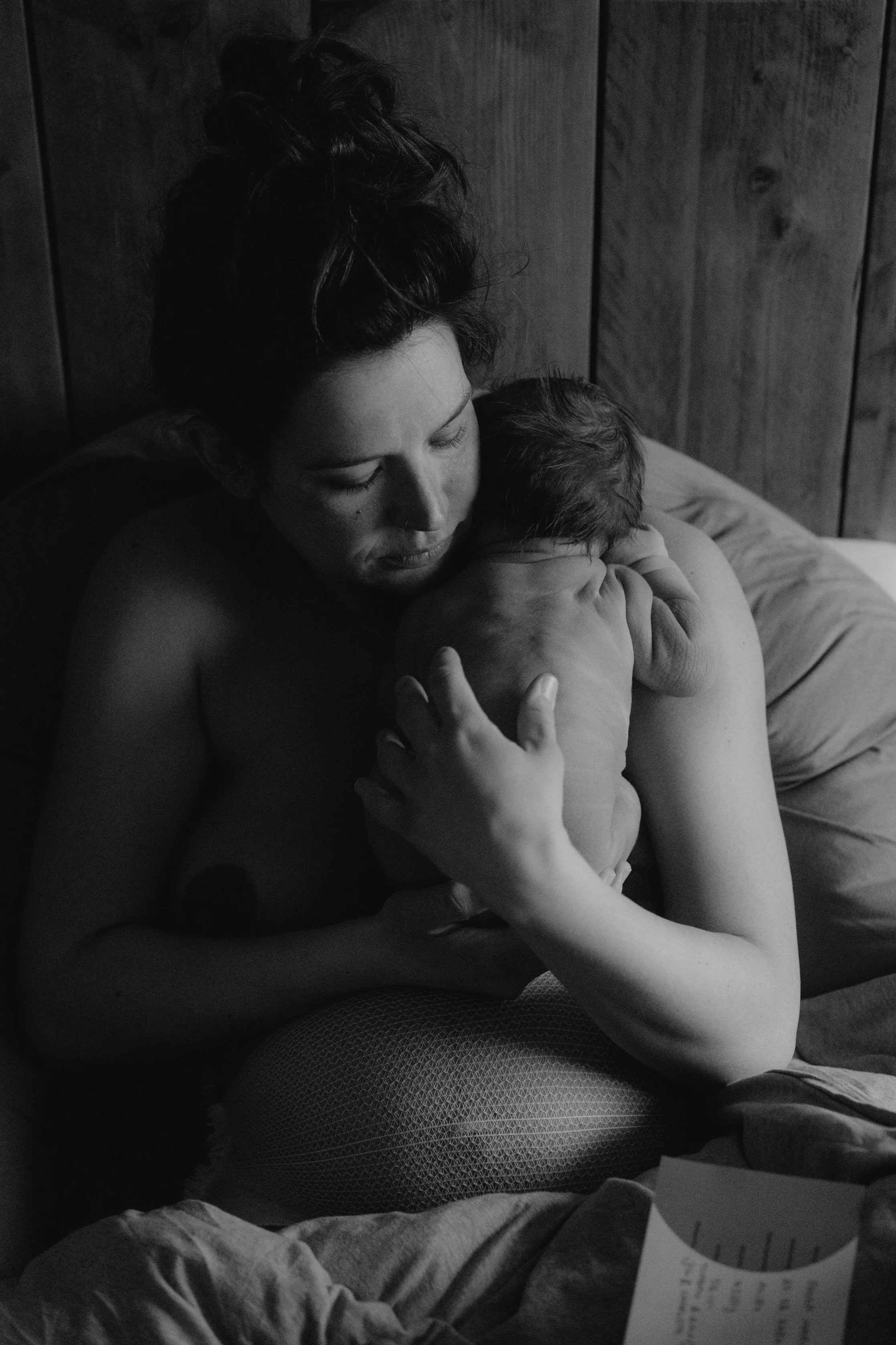 Schwarz-weiß-Foto einer Frau, die ihr neugeborenes Baby stillt auf einem Bett in einem Raum mit Holzverkleidung