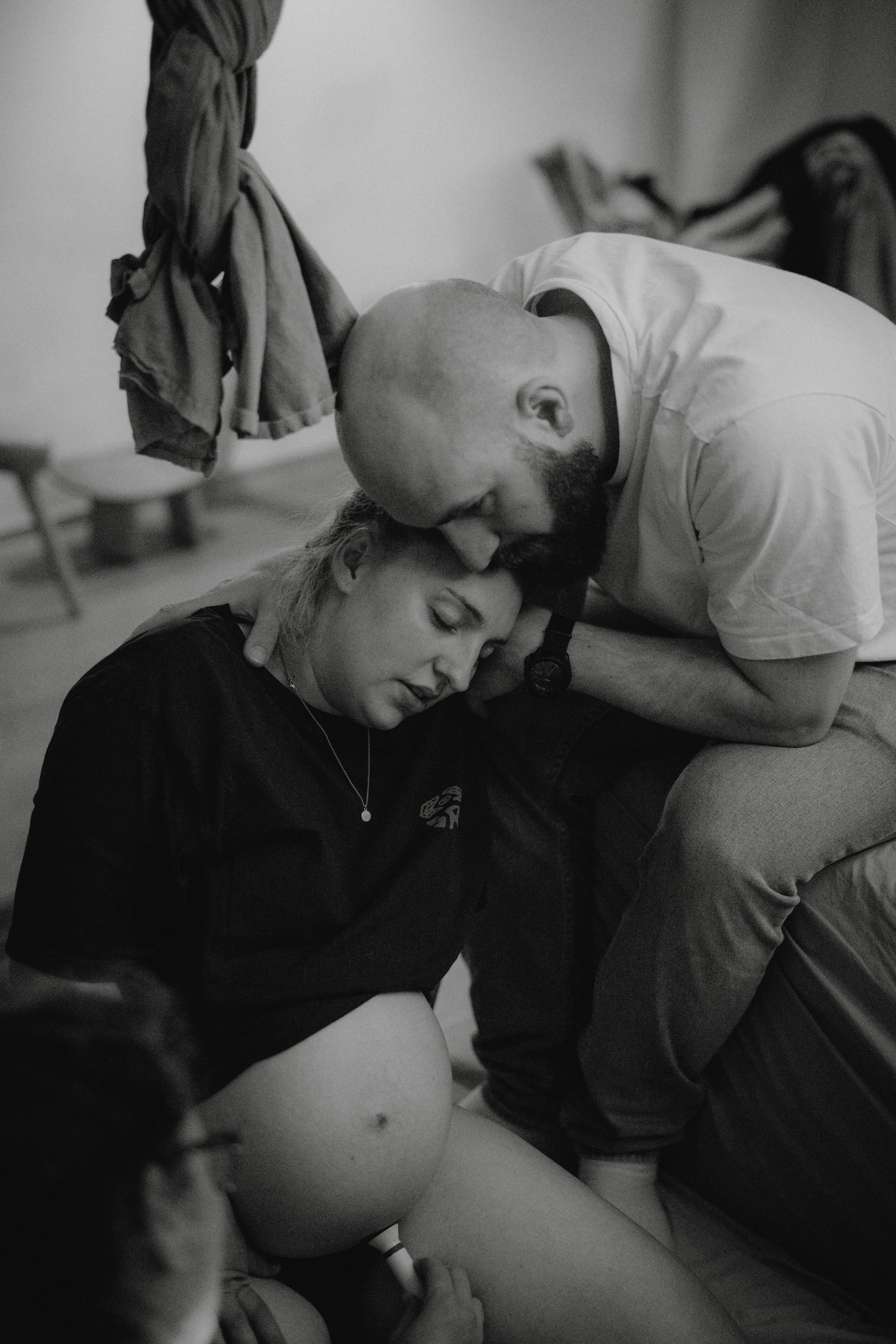 Eine schwangere Frau liegt auf dem Boden und bekommt eine Gebetshaltung von einem Mann, während eine weitere Person im Vordergrund zuschaut.