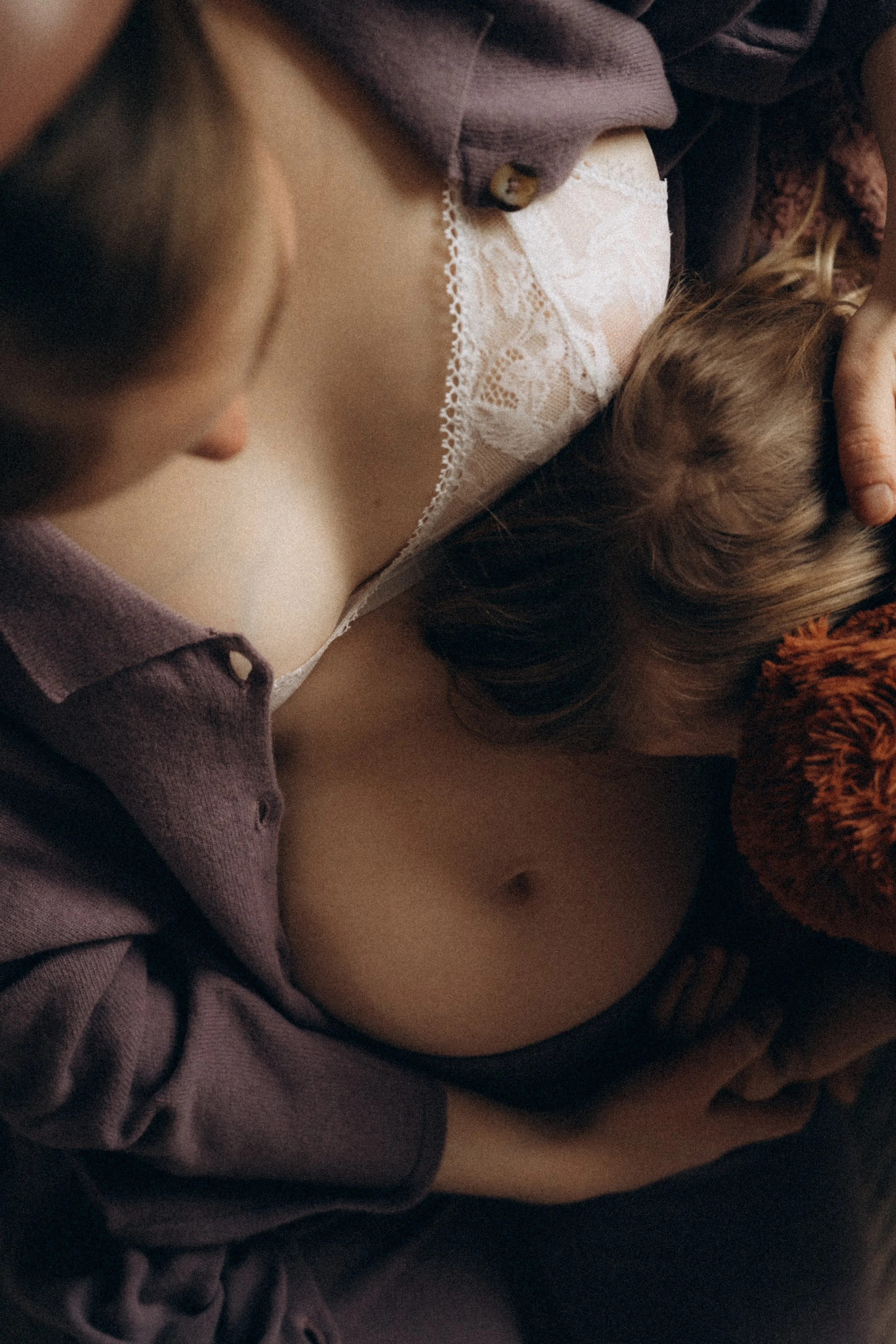 Nahaufnahme eines jungen Paares, das intim kuschelt. Sie liegt auf dem Rücken, trägt Unterwäsche und ein offenes Hemd. Ein Kind kuschelt ebenfalls in der Nähe.