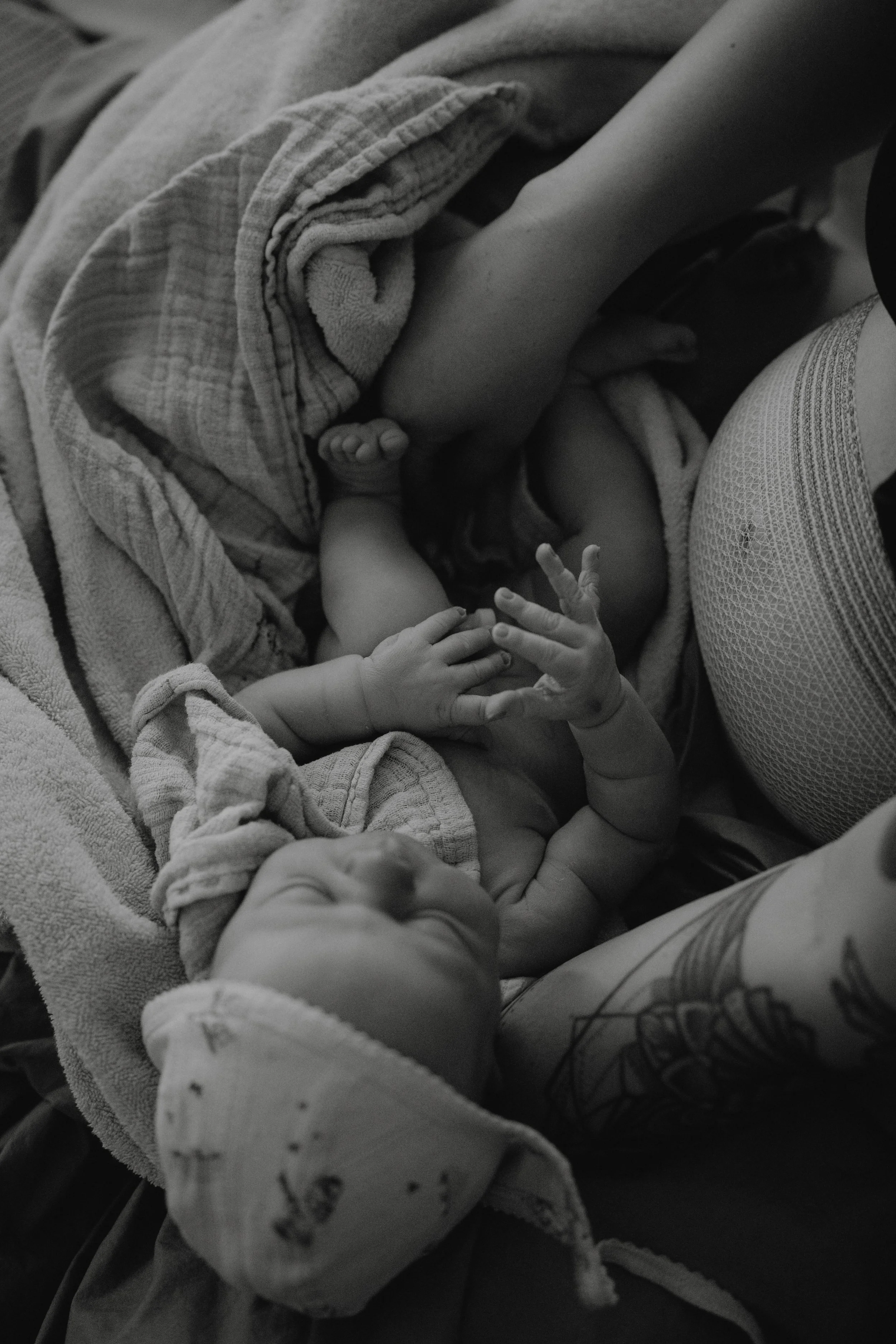 Zwei Babys ruhen auf einer Decke, eines trägt einen Schlafanzug mit Punkten, das andere ist nackt, während eine erwachsene Person sie hält.