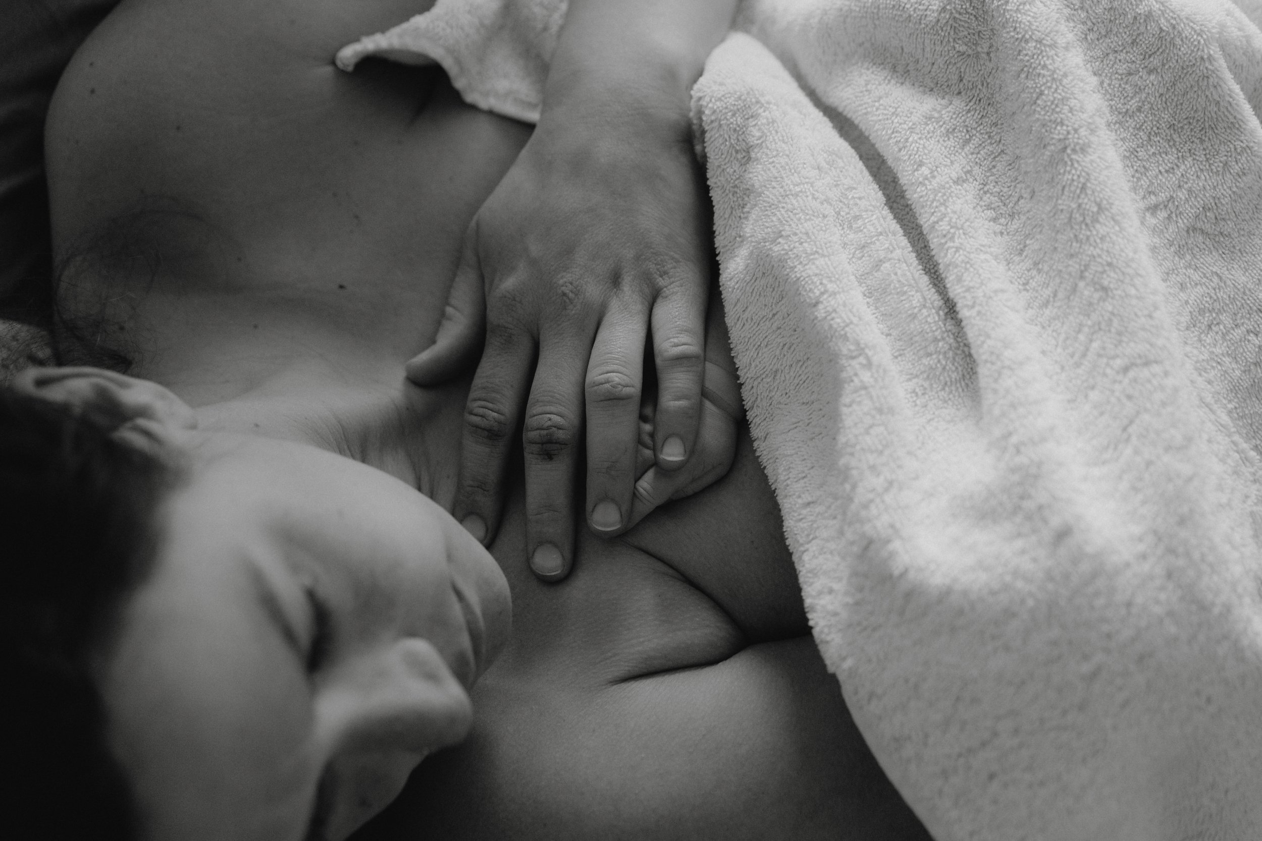 Eine Person liegt auf dem Rücken, während eine andere Person mit der Hand auf ihrer Brust liegt, teilweise mit einem Handtuch bedeckt.