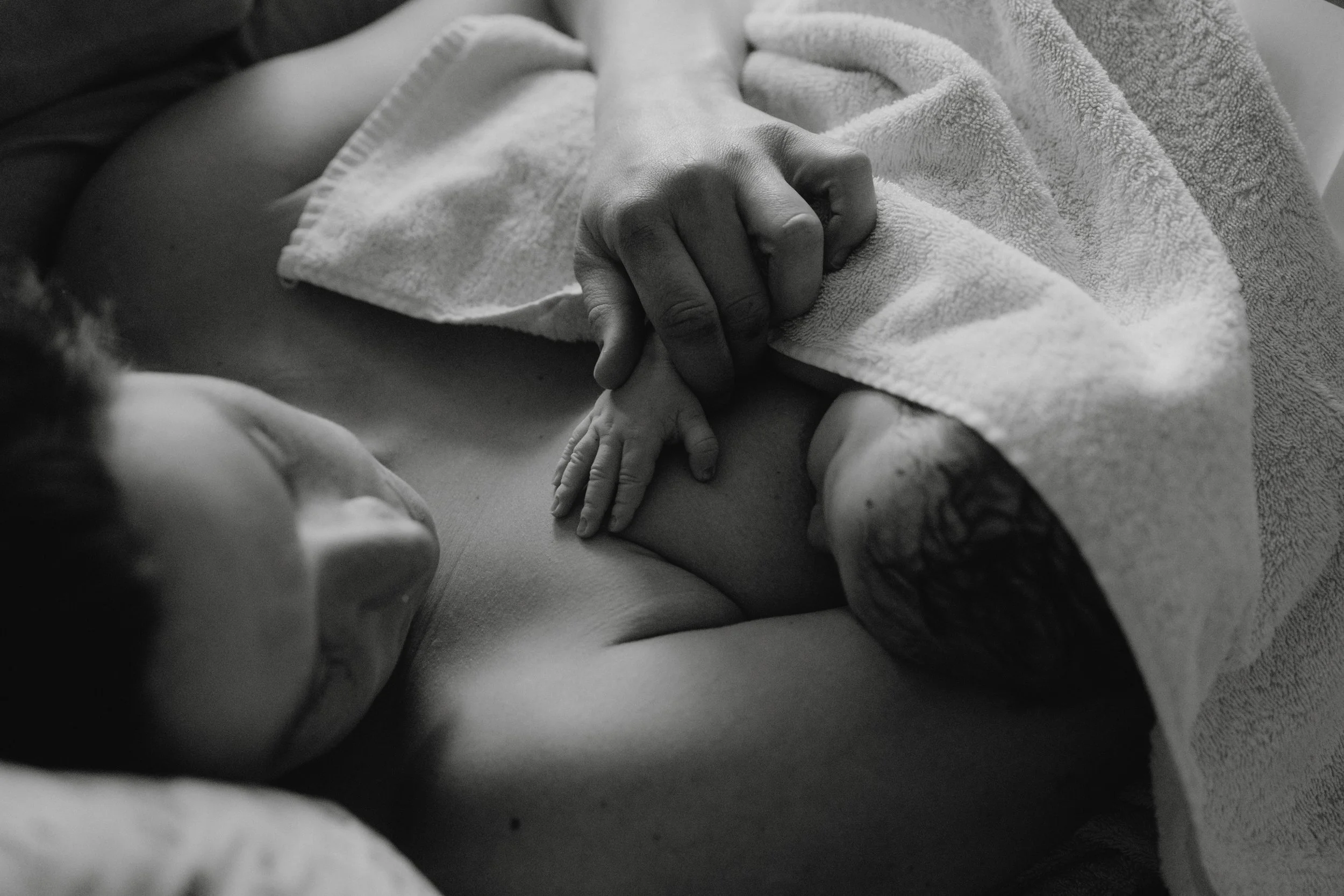 Sternenkinderliebe: Ein Neugeborenes hält die Hand seiner Mutter, die im Krankenhaus liegt, in Schwarz-Weiß aufgenommen. Das Baby liegt nackt auf dem Bauch der Mutter, während diese eine Hand auf das Baby legt.