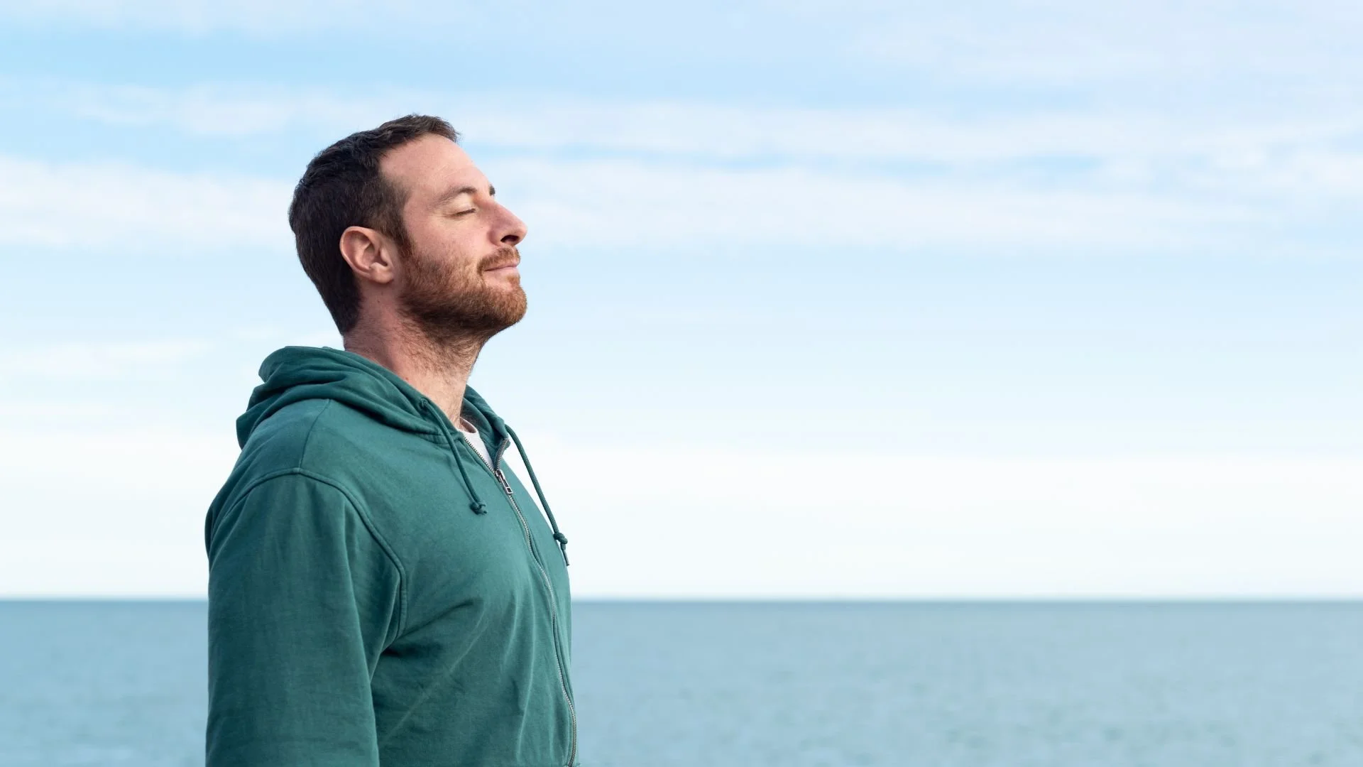 Calm midlife man standing by sea breathing in fresh air