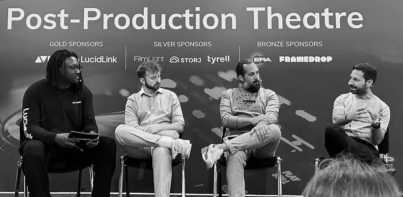 Four men seated on a stage at a post-production theatre panel discussion. The backdrop displays sponsor logos and the words 'Post-Production Theatre'.