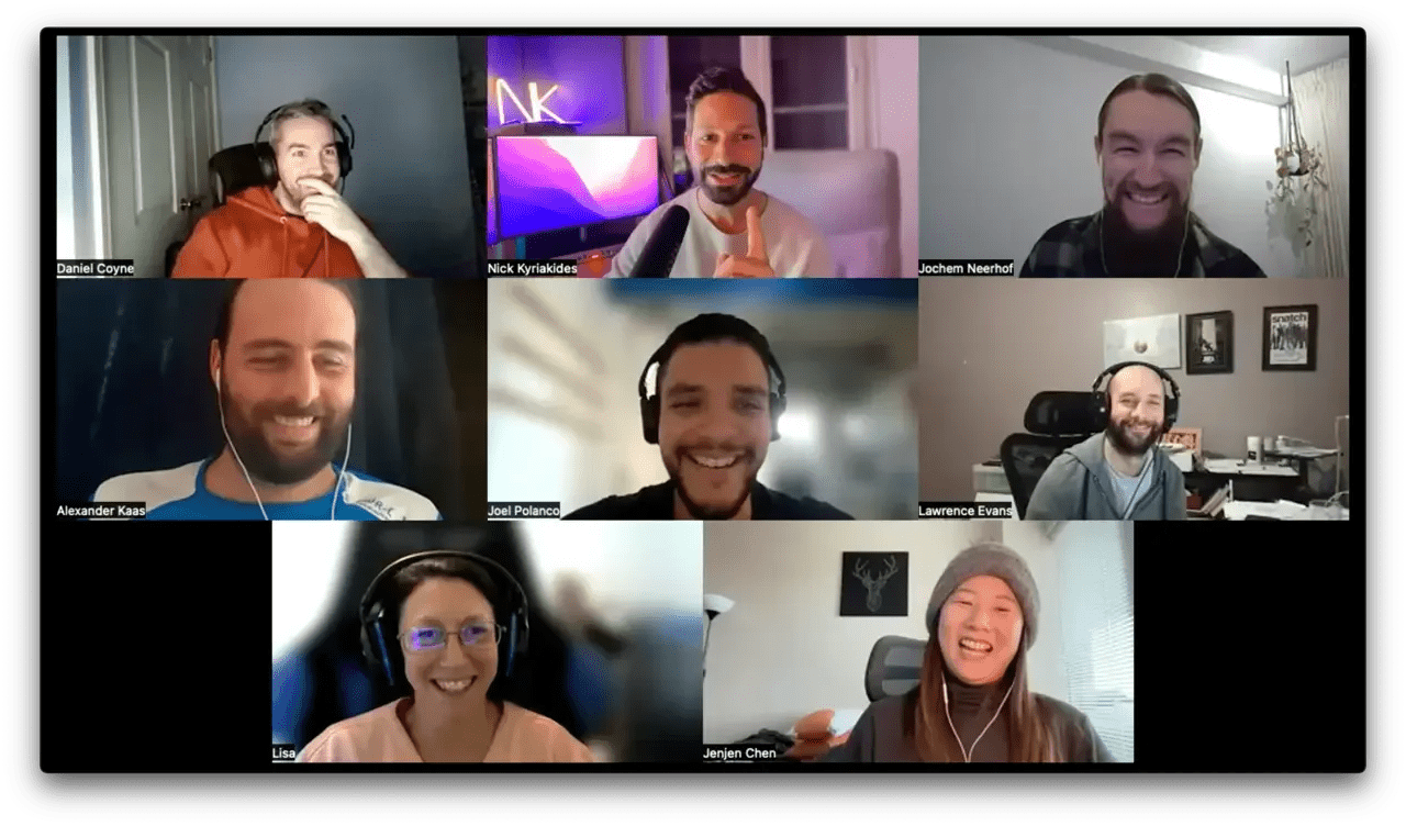 Group video call with nine smiling people in a grid, wearing headphones and casual clothing, in various home office settings.