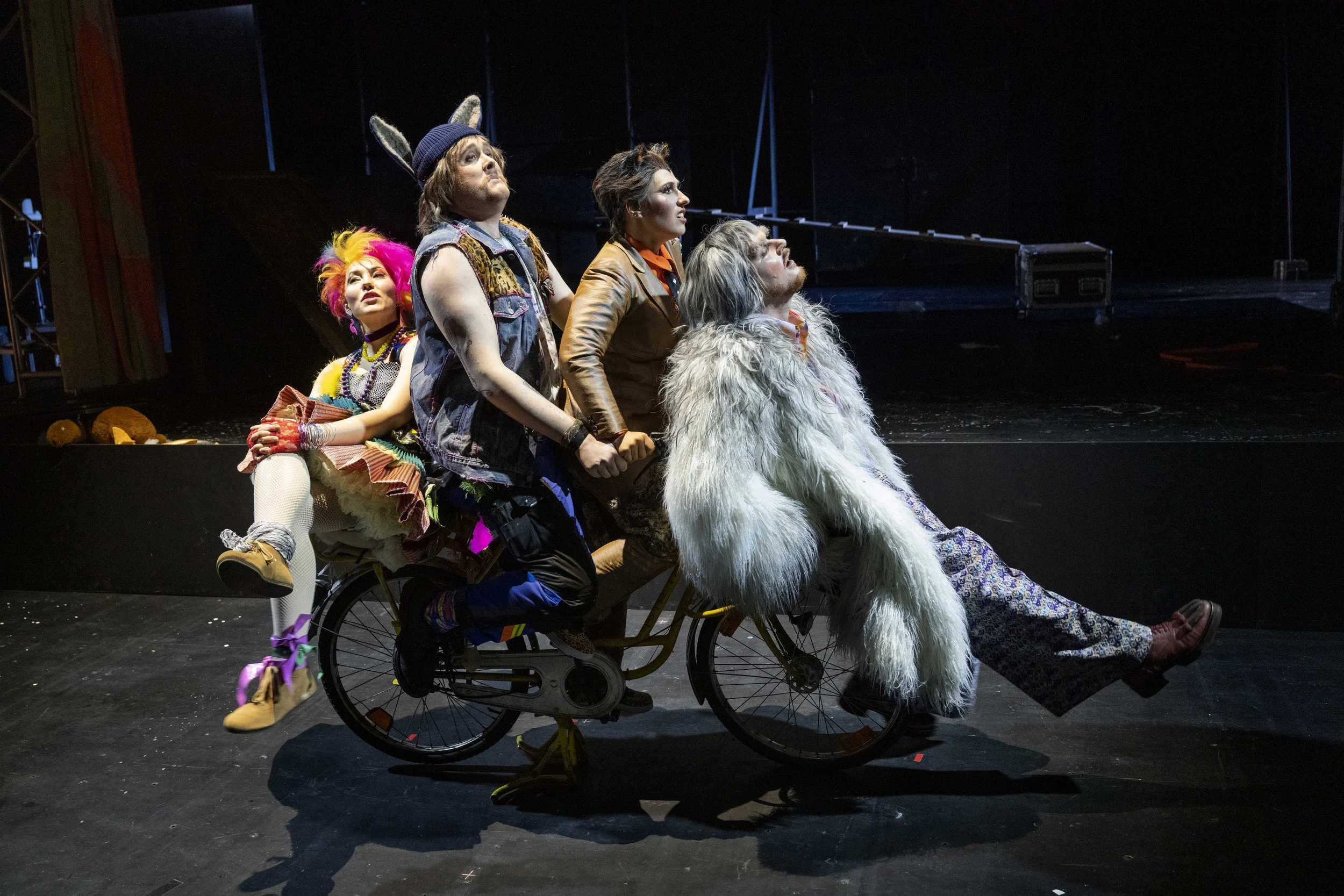 Group of five performers on stage in colorful costumes, with one performing in a wheelchair, looking upward with focused expressions.