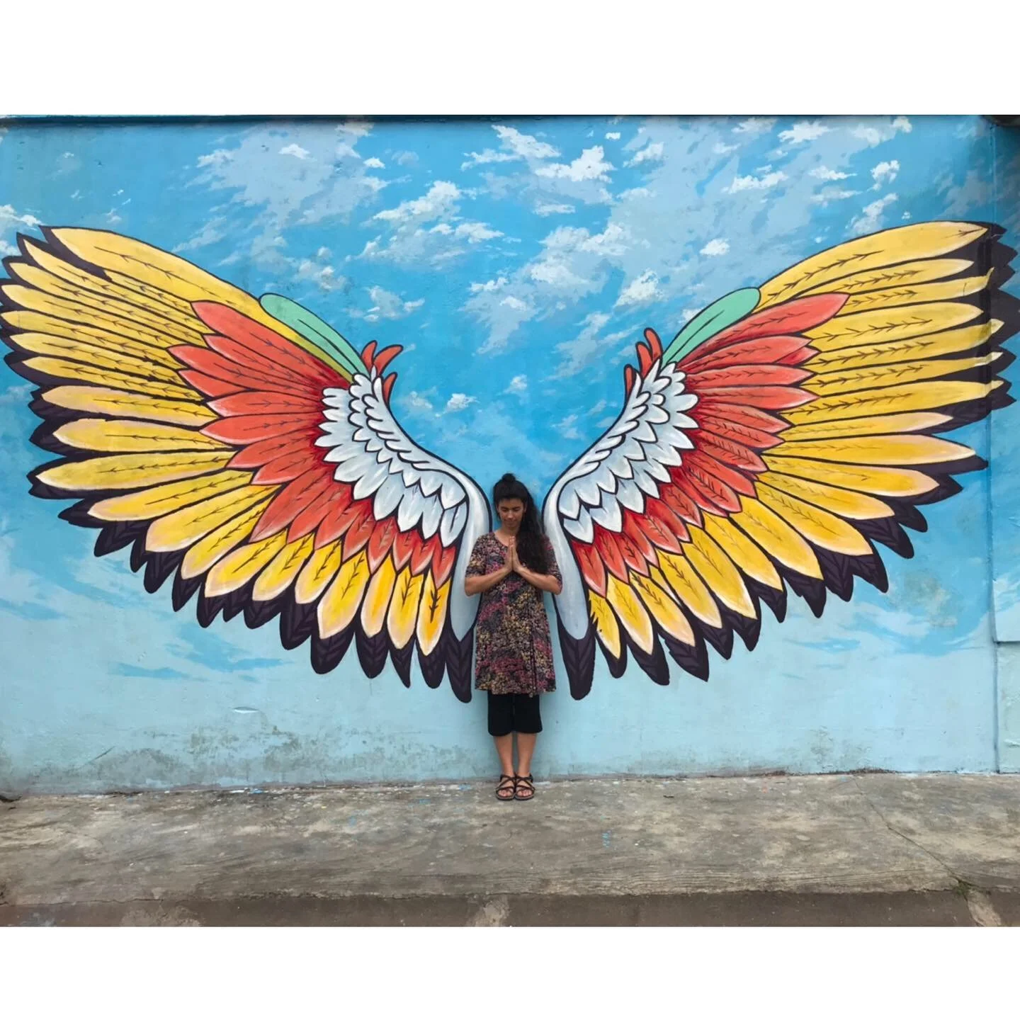 An artist stands in front of a mural with wings 