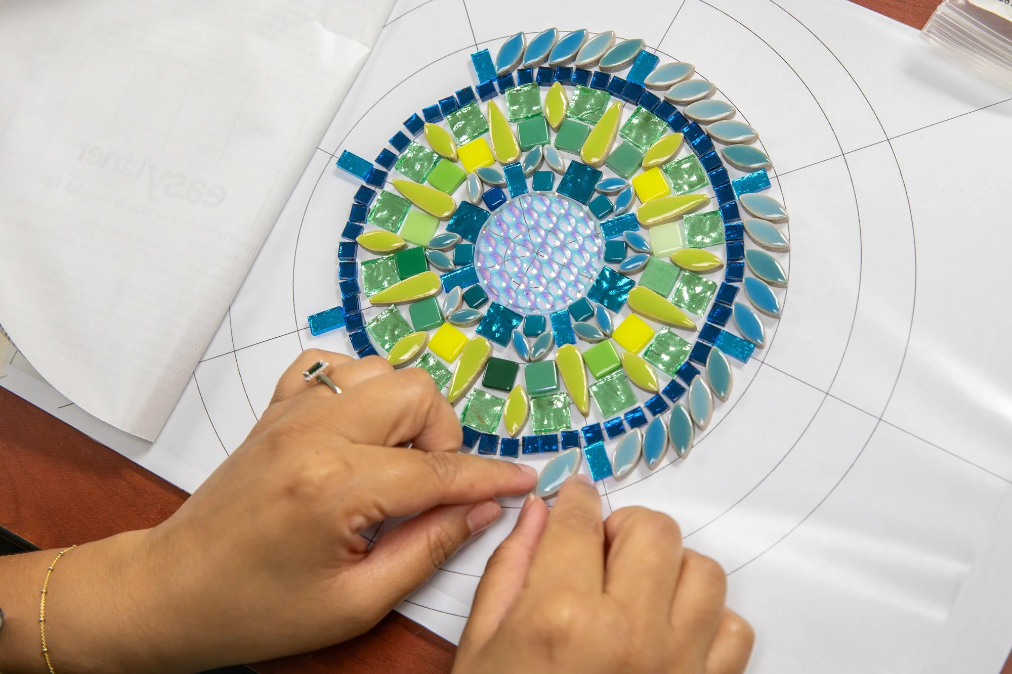 hands create a green and blue mosaic mandala 