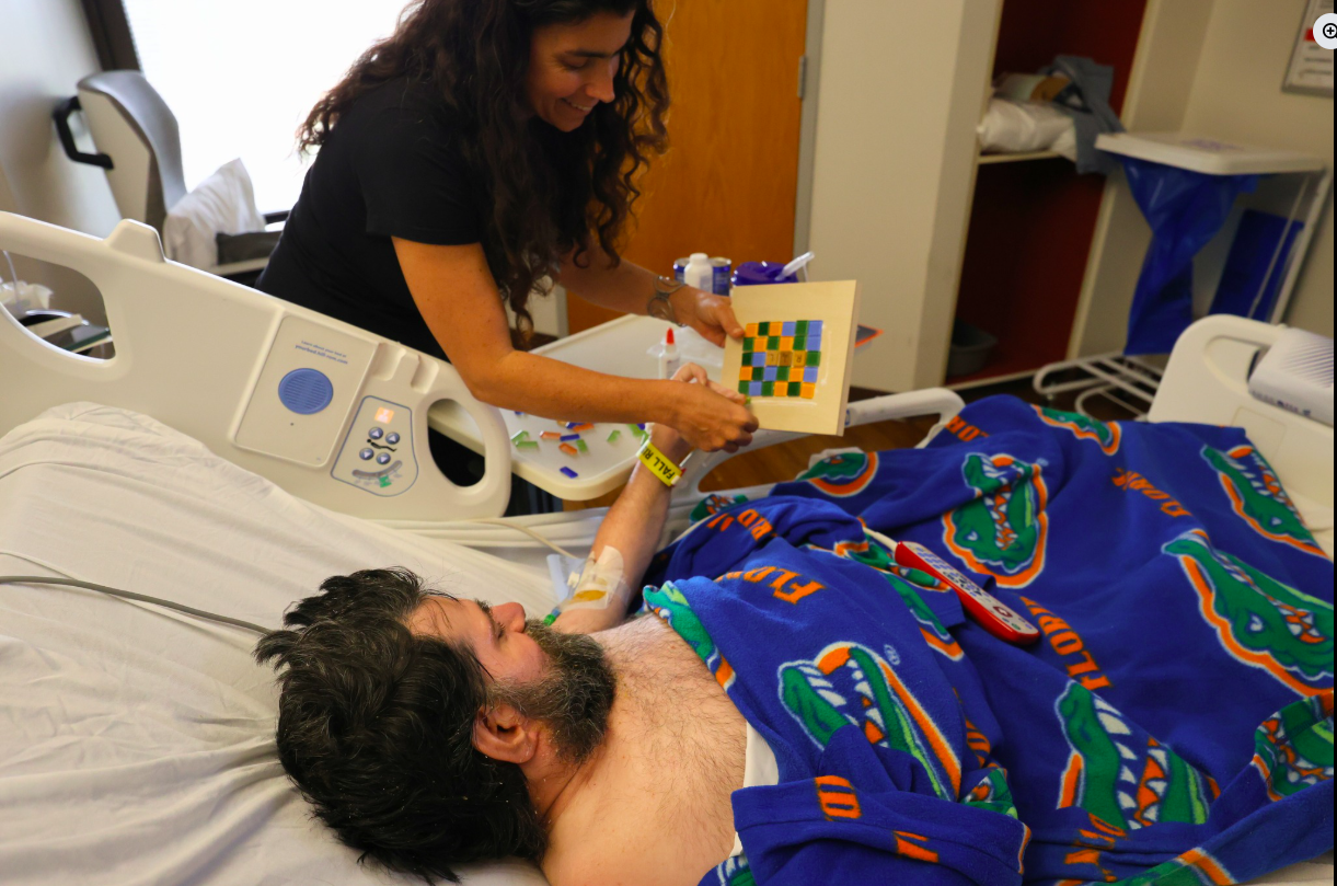 A woman helps a hospitalized patient make a mosaic