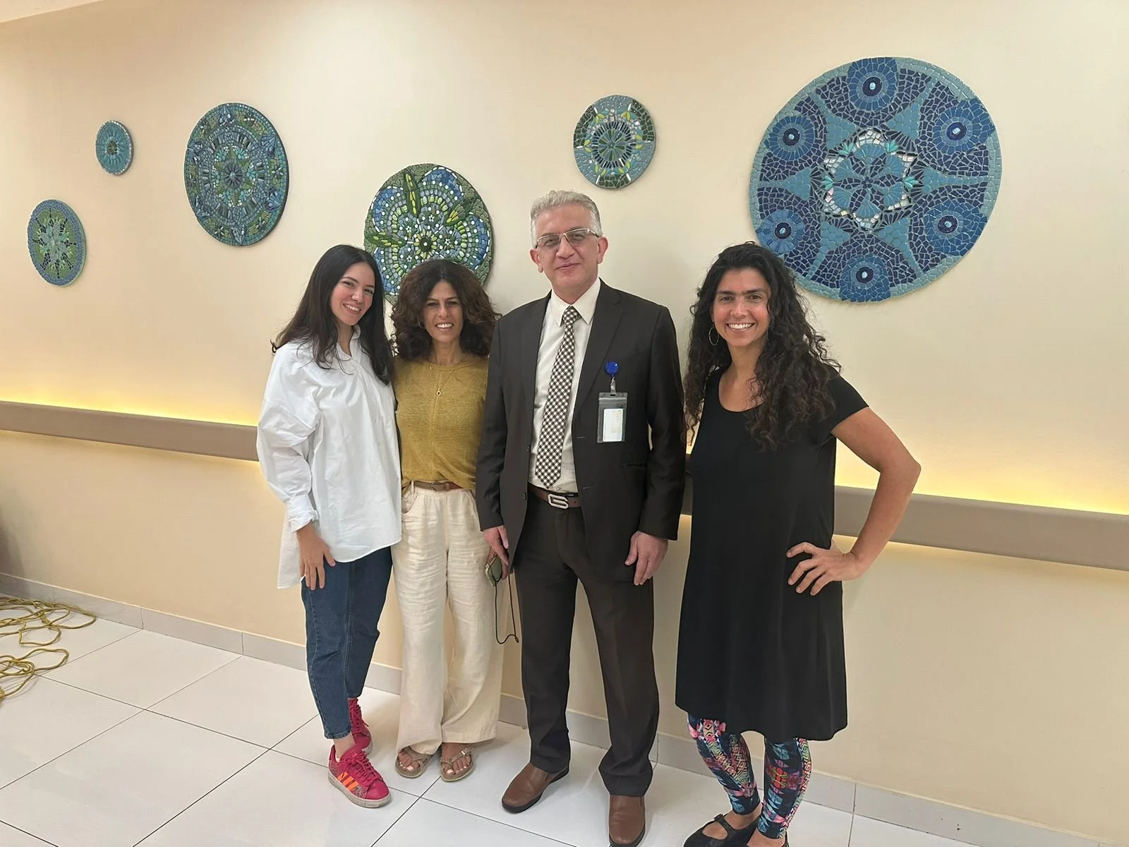 Artists stand with hospital executive in front of mosaic mural 