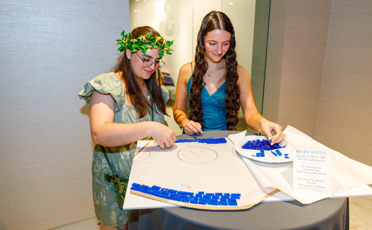 Two young women work on a mosaic with blue tiles 