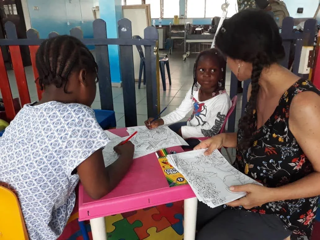 Children work on coloring pages as an adult looks on 