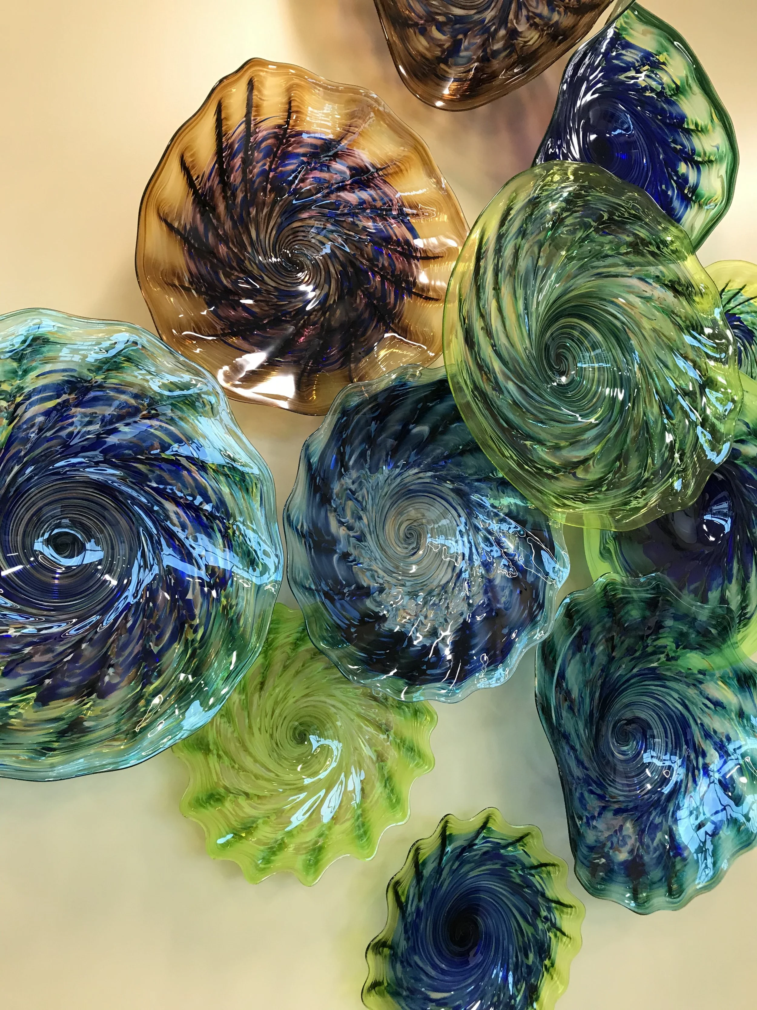 close up of hand blown glass platters in greens blues and browns